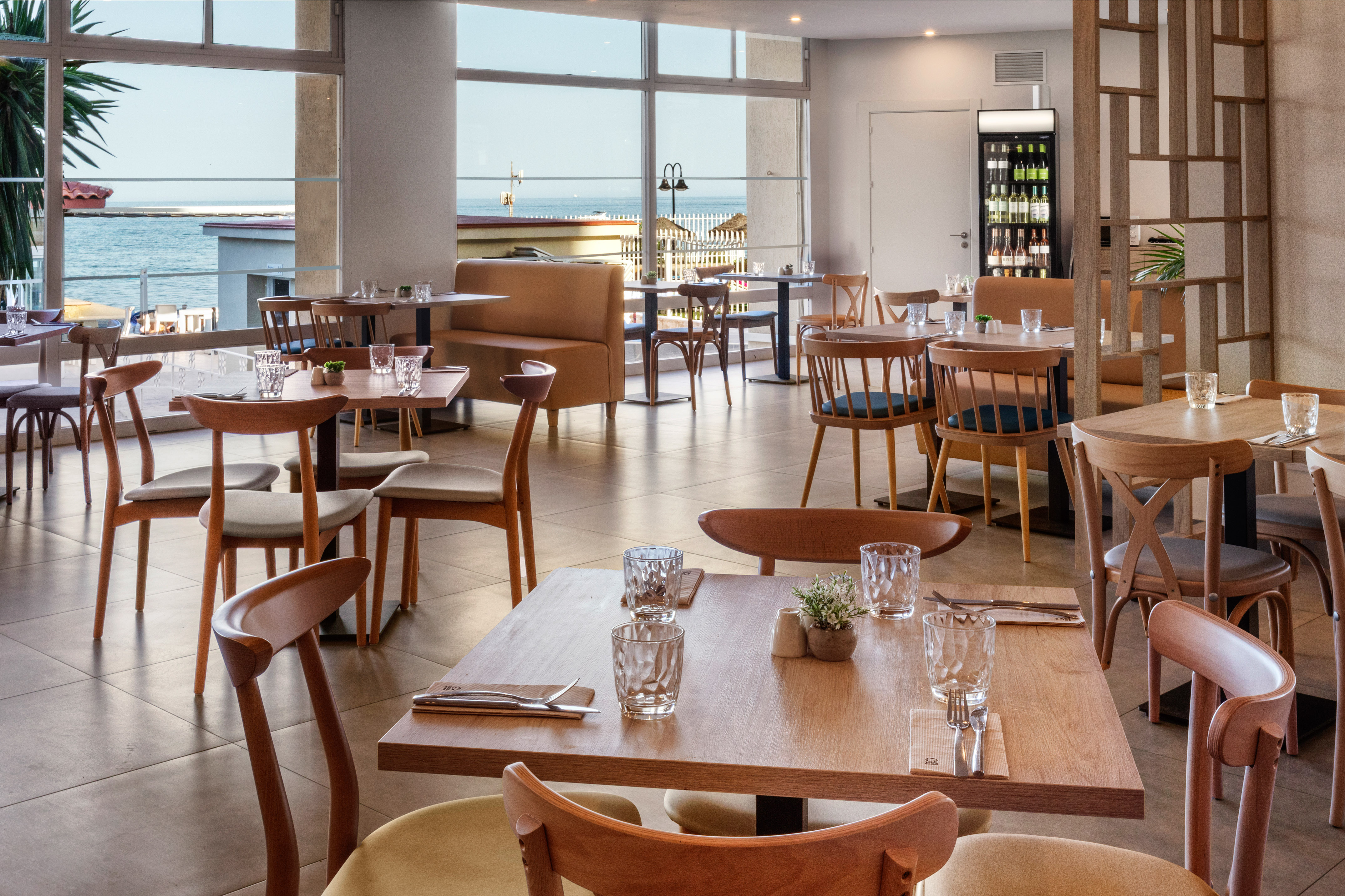 Modern beachfront restaurant interior with wooden tables and panoramic sea view.