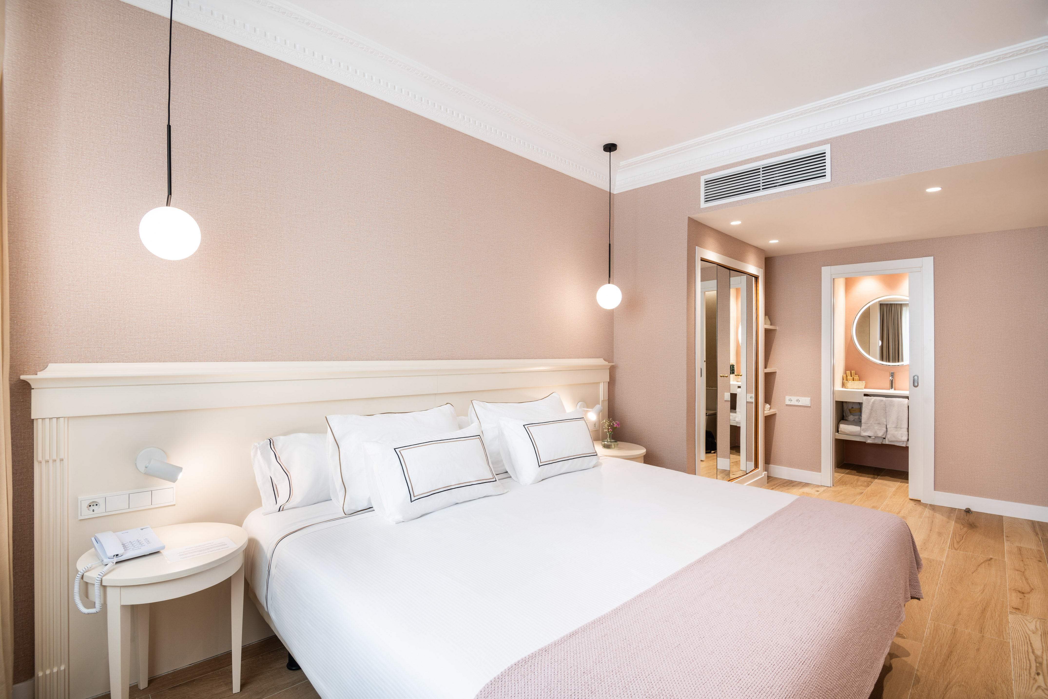 Pink hotel bedroom with white bed, wooden floor, and en-suite bathroom.