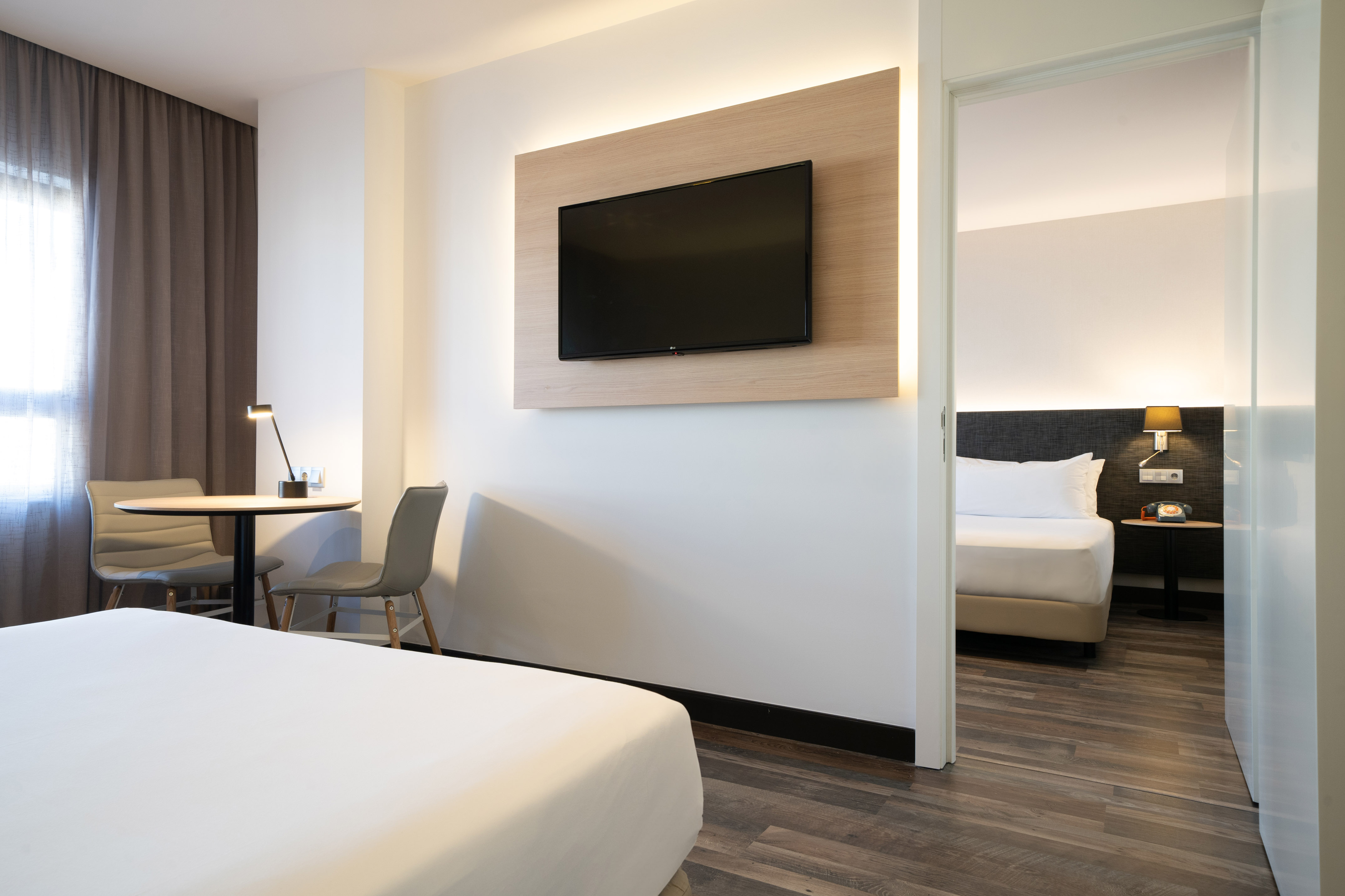 Modern hotel suite with living area, mounted TV, and visible bedroom.
