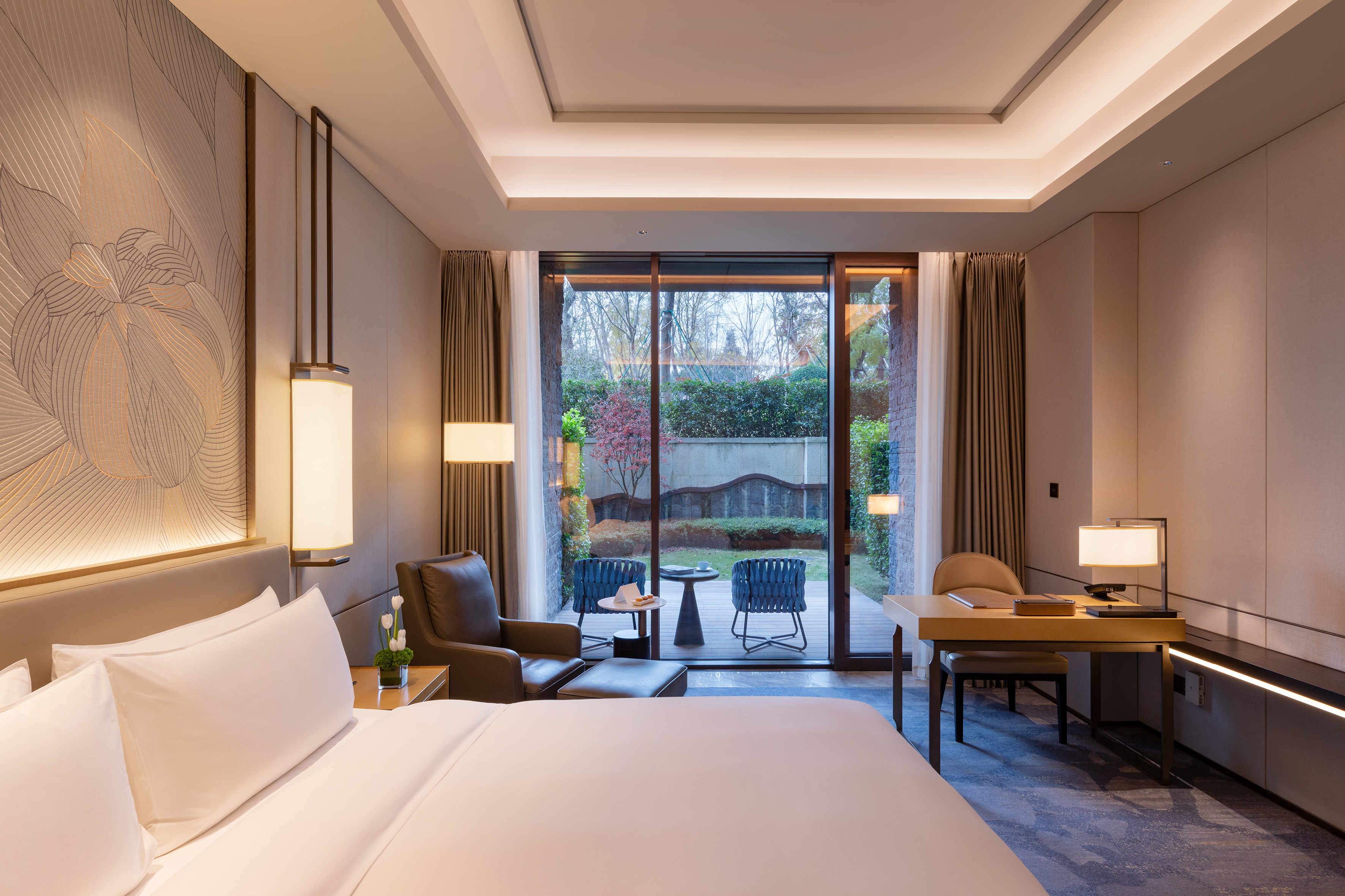 Luxury hotel suite with private garden patio, king bed, and modern workspace.