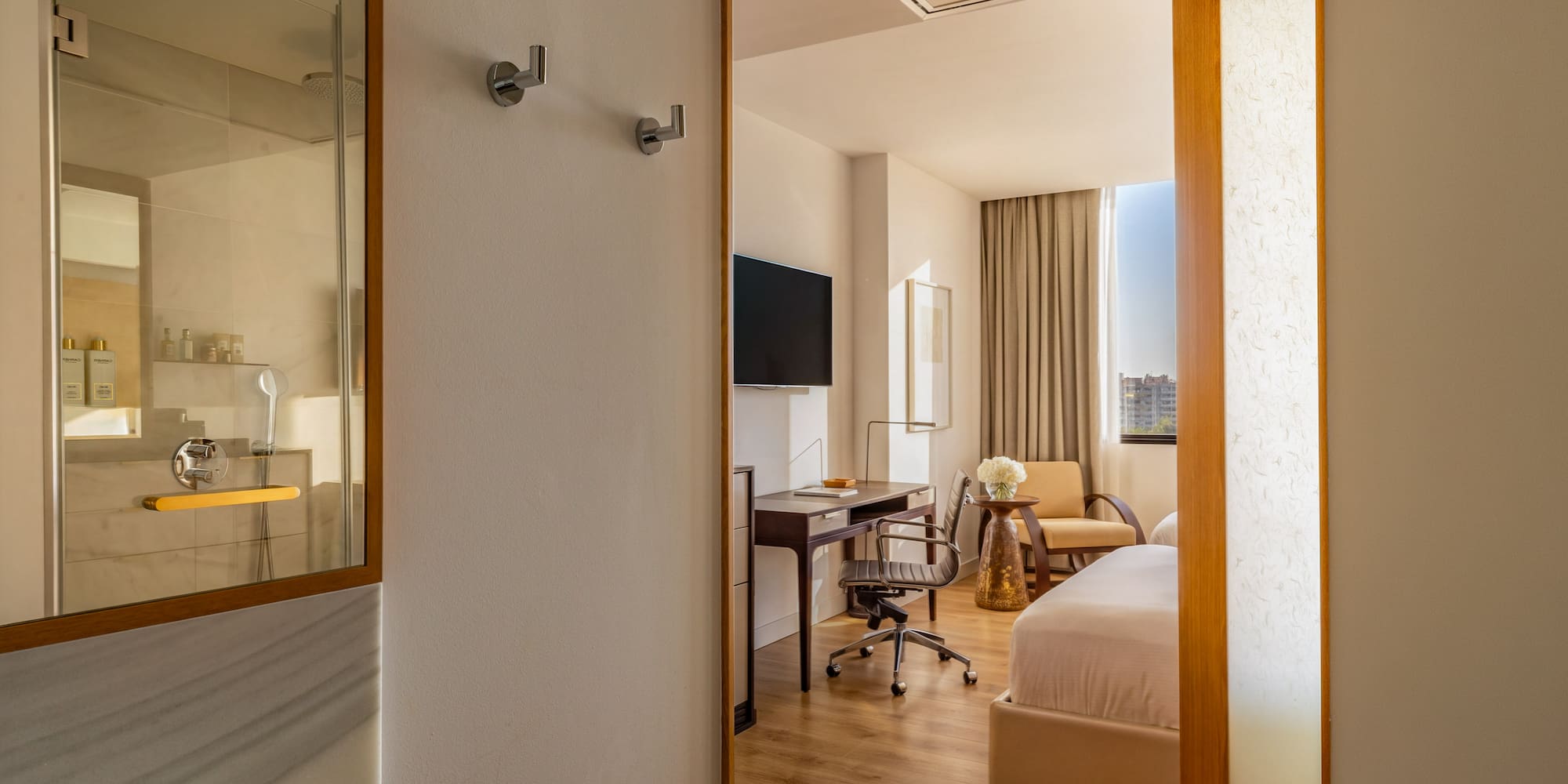 Modern hotel room with bed, work desk, wall TV, and shower.
