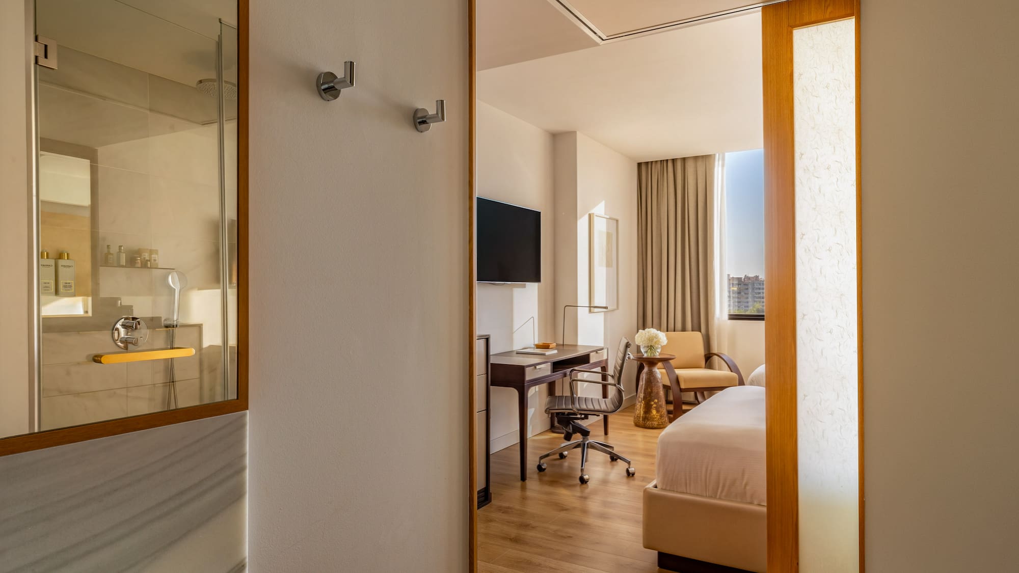 Modern hotel room with bed, work desk, wall TV, and shower.