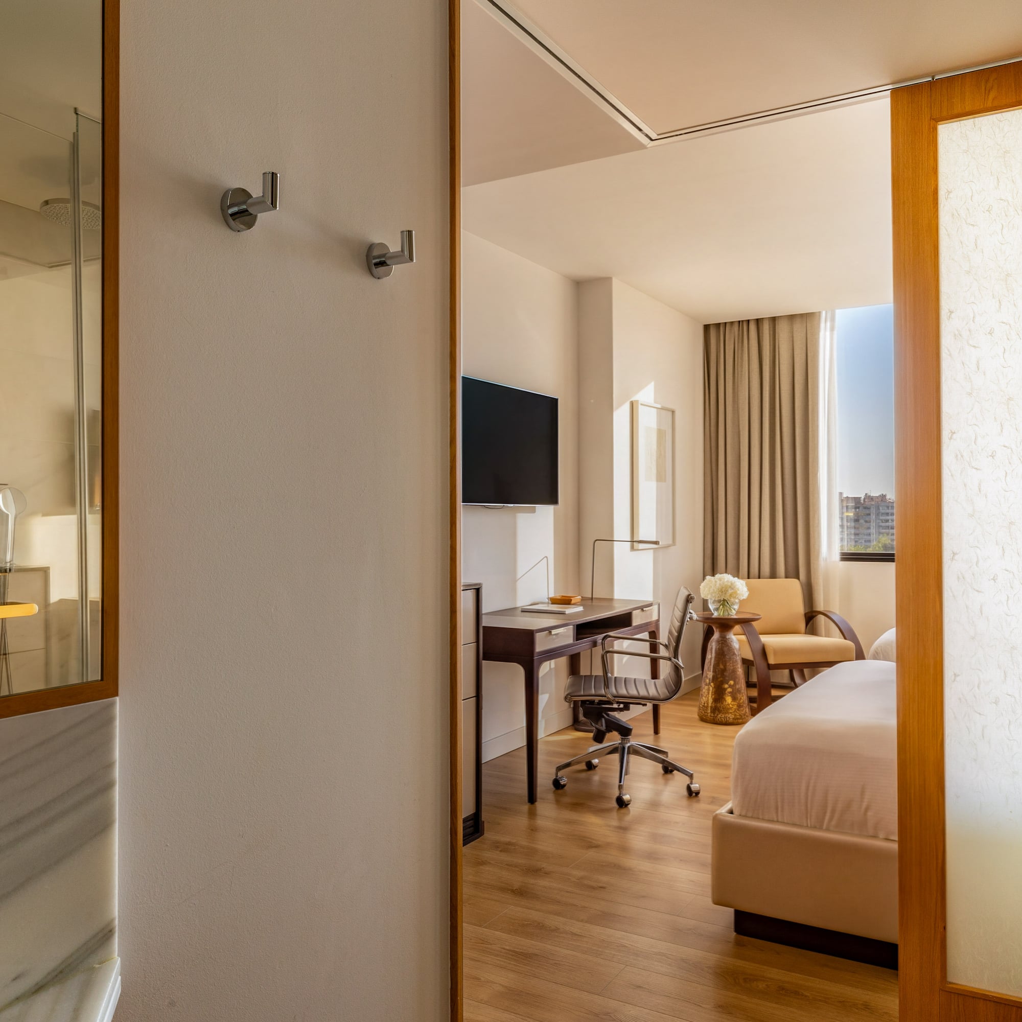 Modern hotel room with bed, work desk, wall TV, and shower.