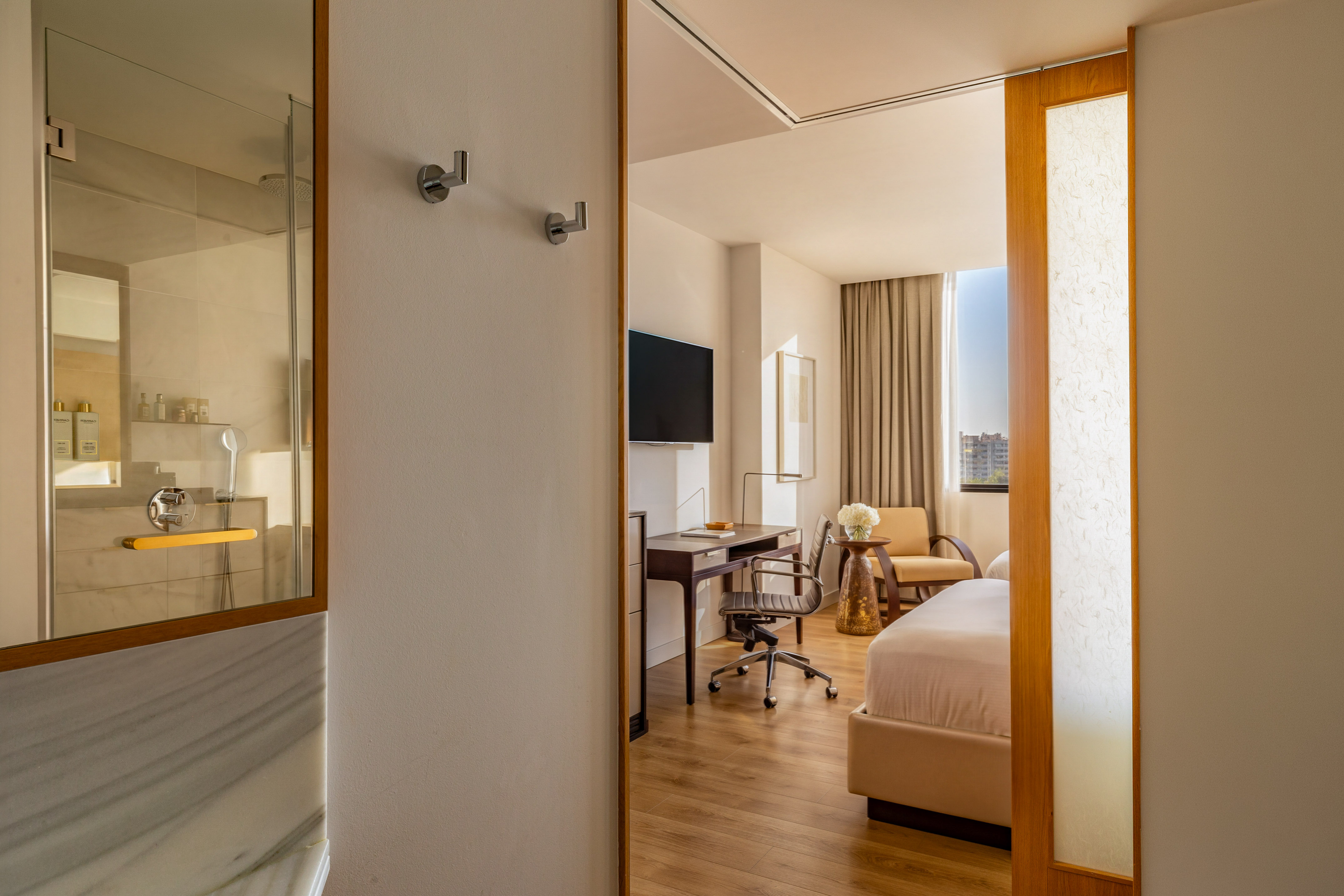Modern hotel room with bed, work desk, wall TV, and shower.