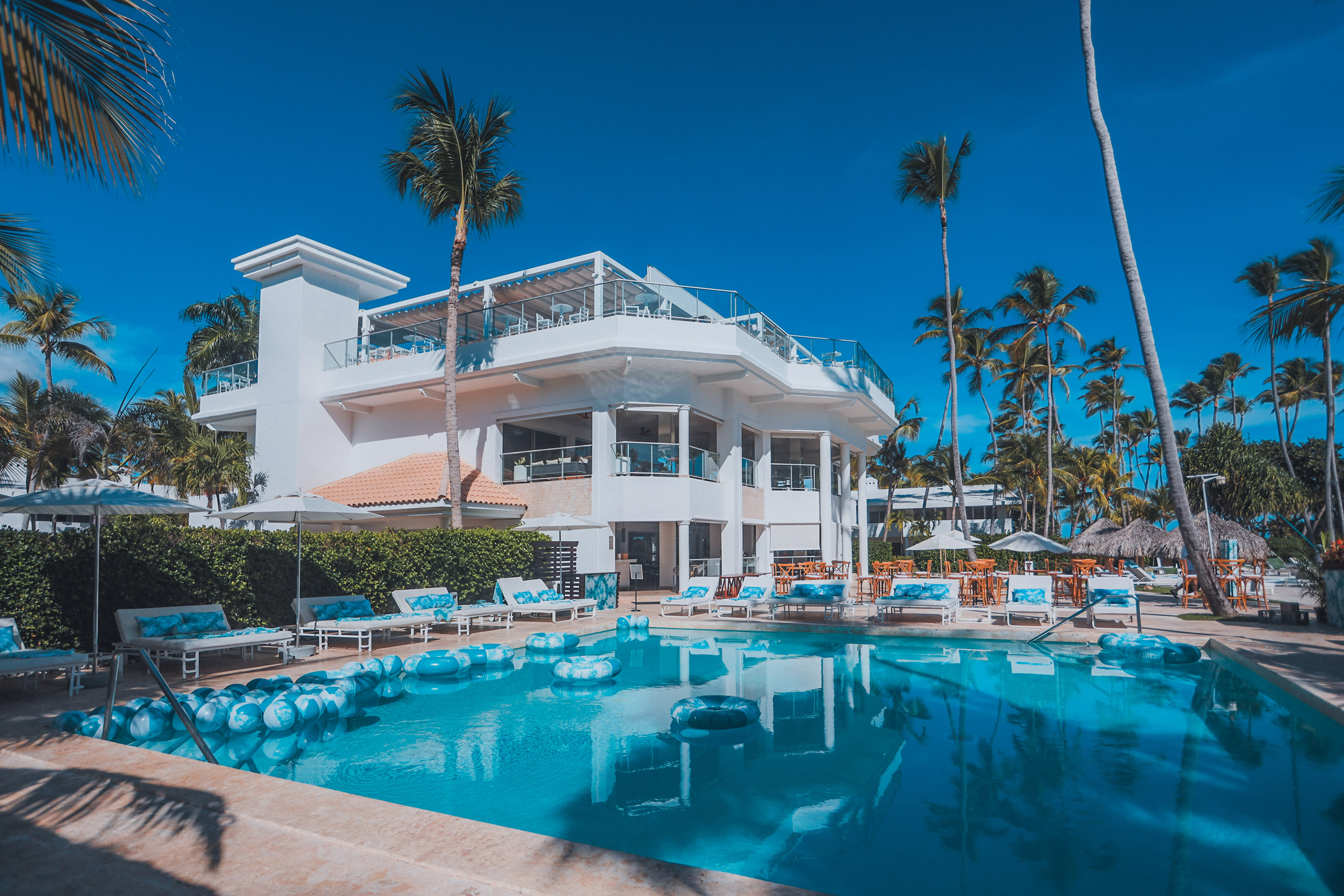 Tropical resort with white building, blue swimming pool, and palm trees.