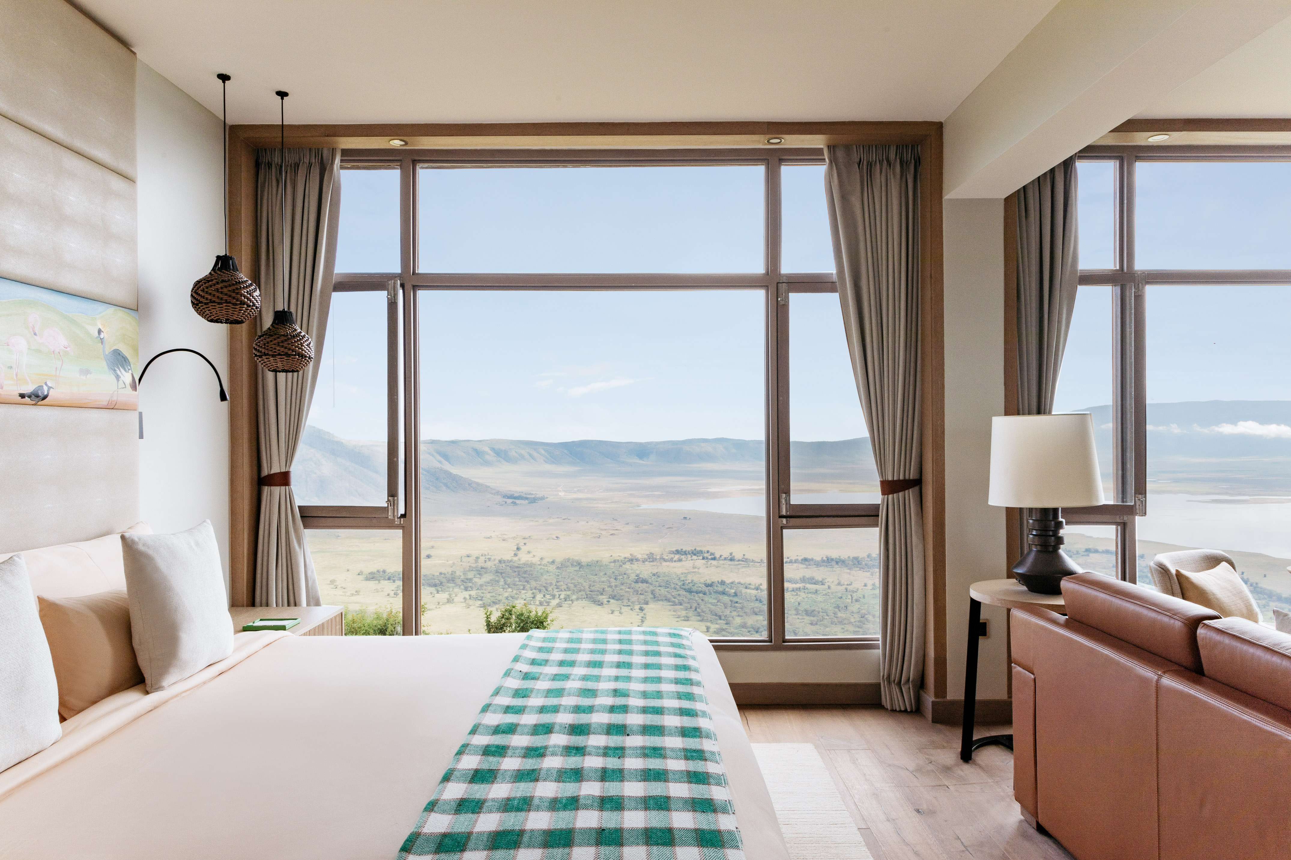 Modern hotel bedroom with a large window overlooking a scenic savanna crater.