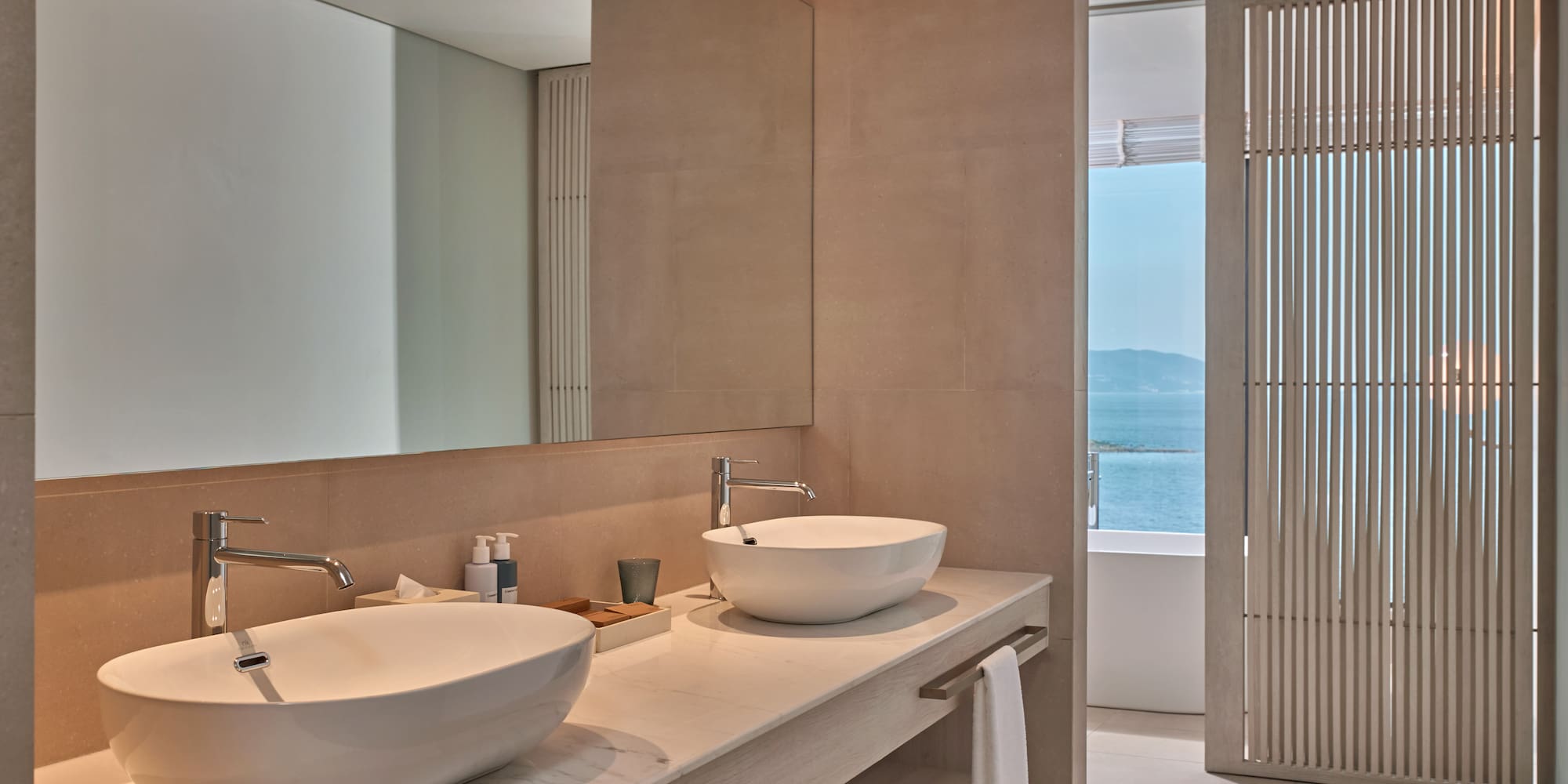 Modern bathroom vanity with double sinks, large mirror, and ocean view.