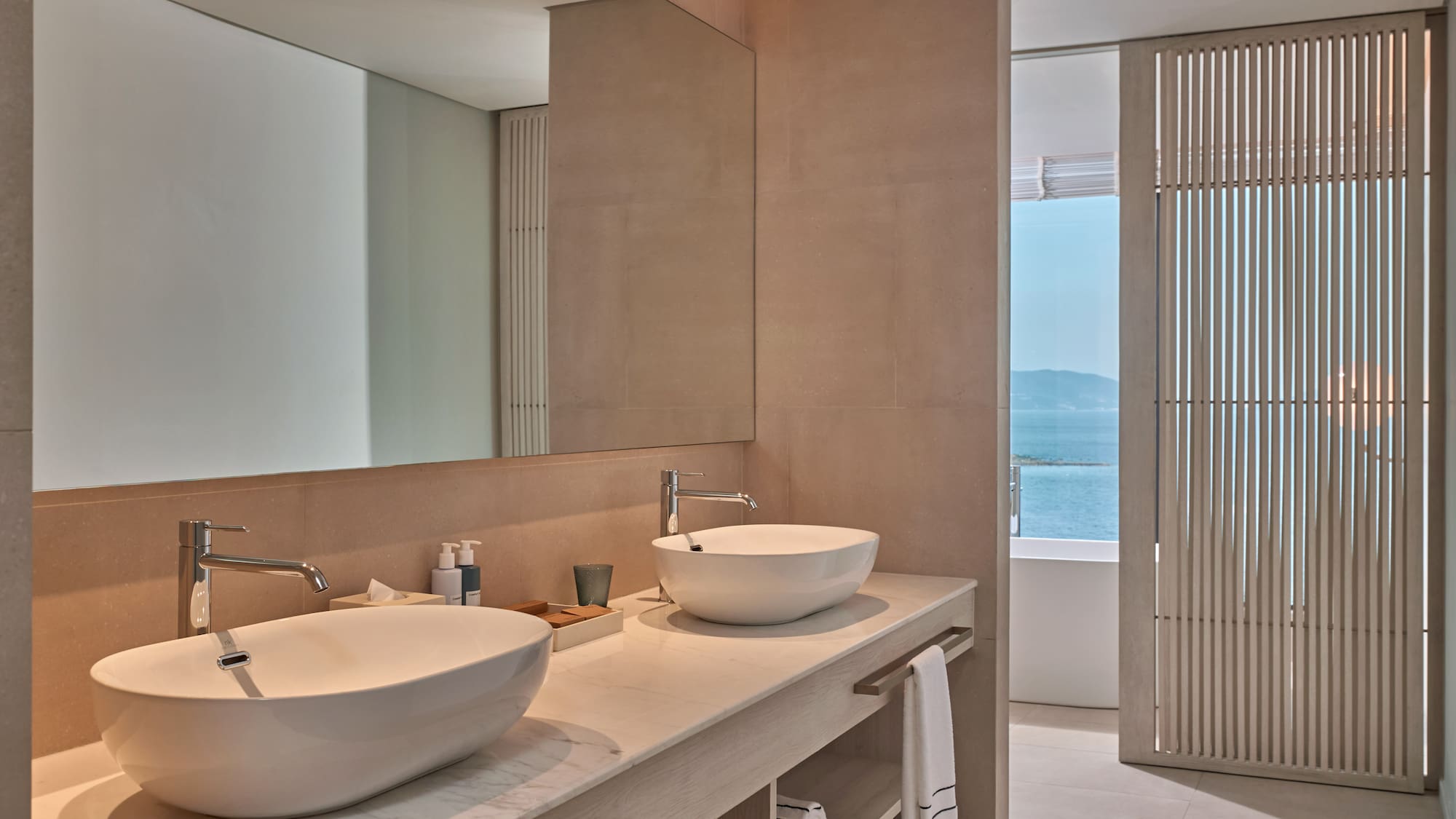 Modern bathroom vanity with double sinks, large mirror, and ocean view.