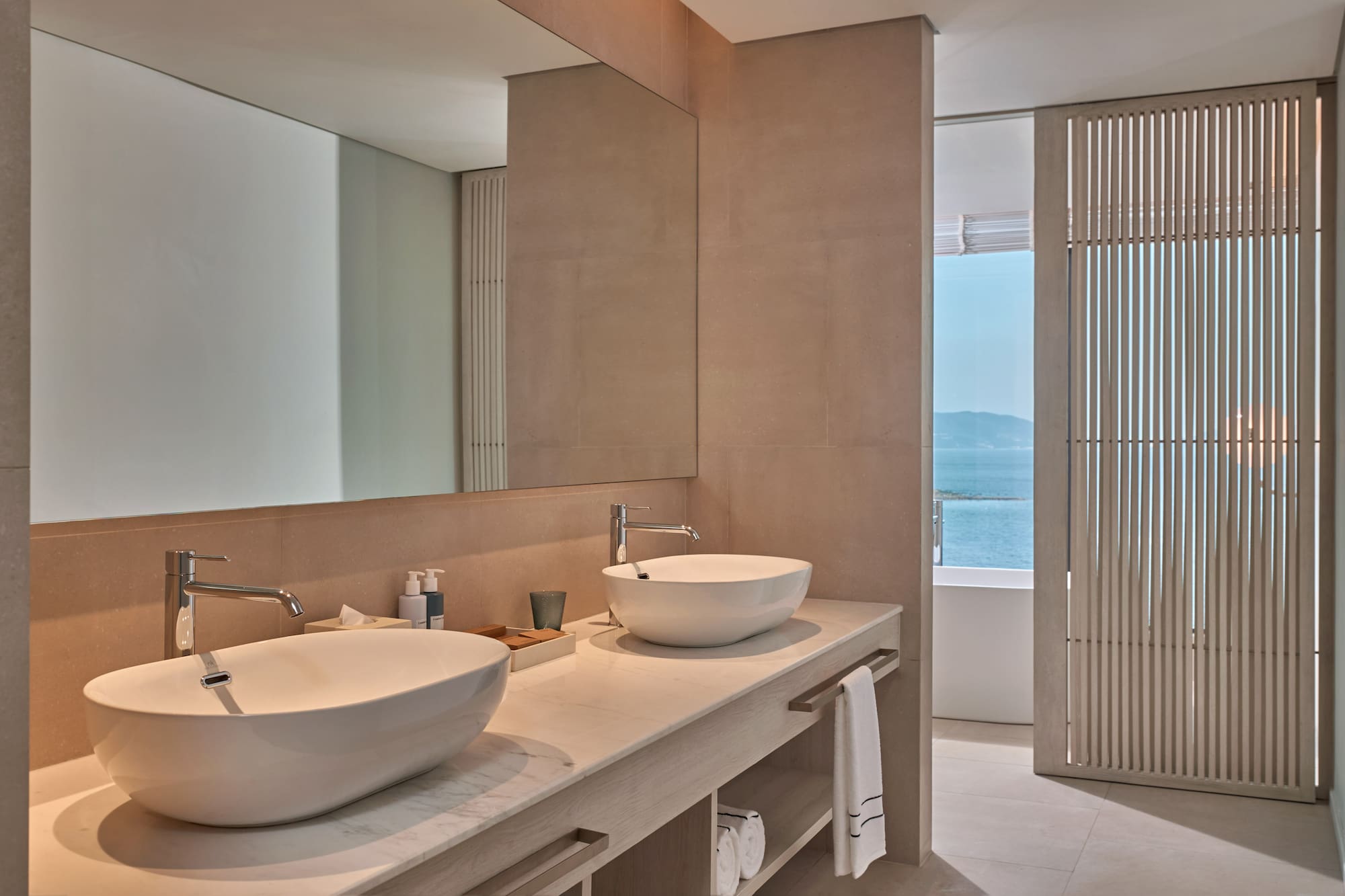 Modern bathroom vanity with double sinks, large mirror, and ocean view.