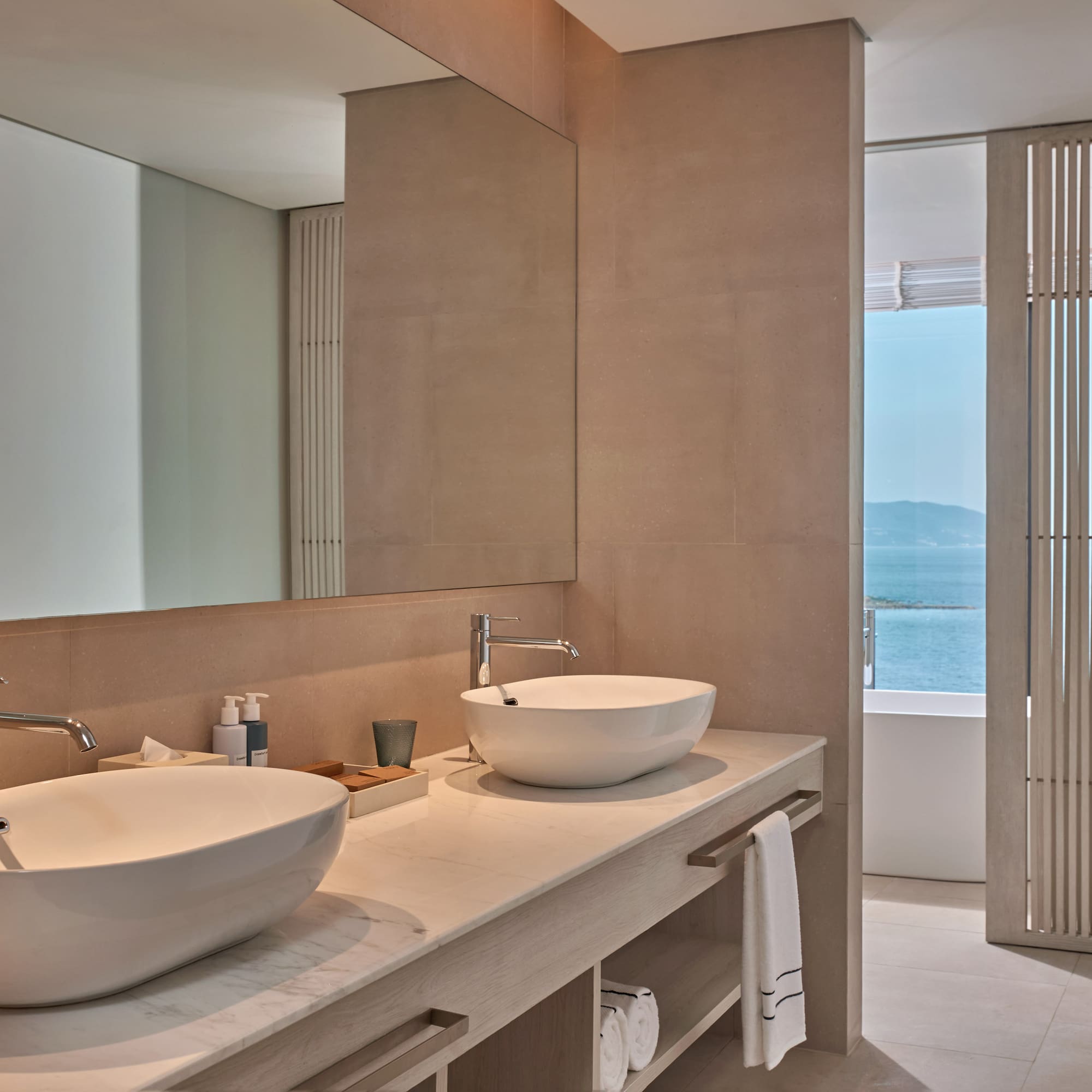 Modern bathroom vanity with double sinks, large mirror, and ocean view.