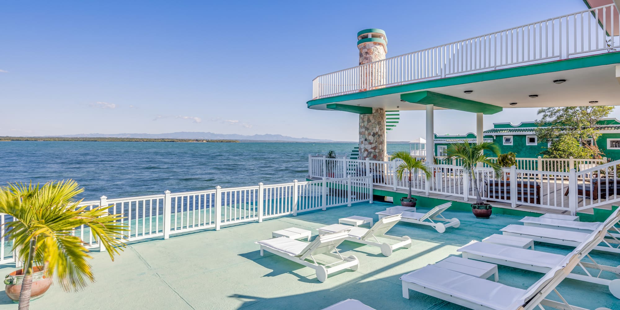 a deck with chairs and a white railing overlooking the water
