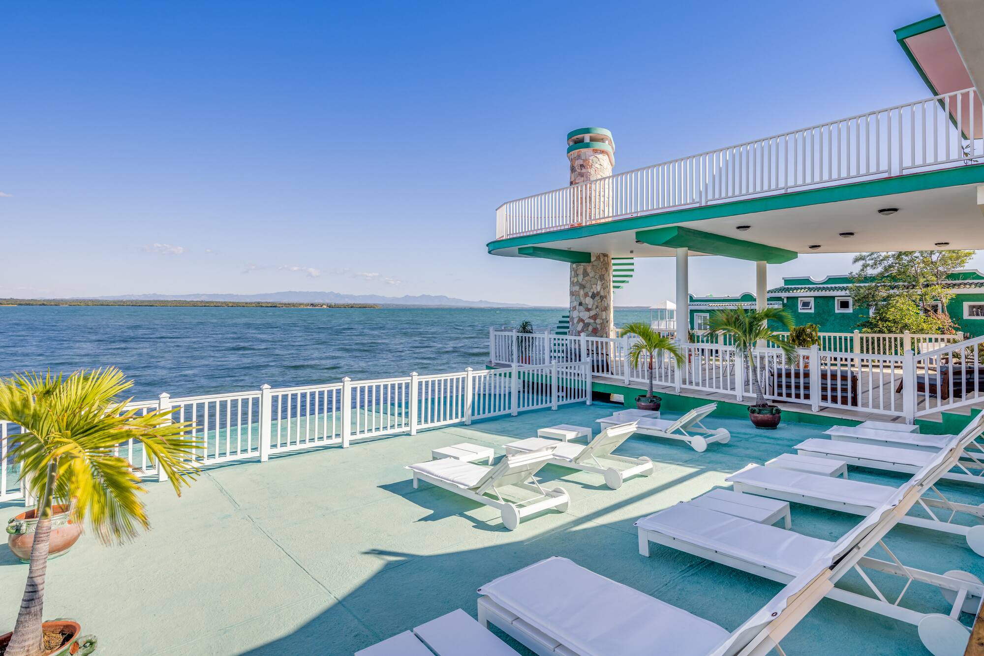a deck with chairs and a white railing overlooking the water