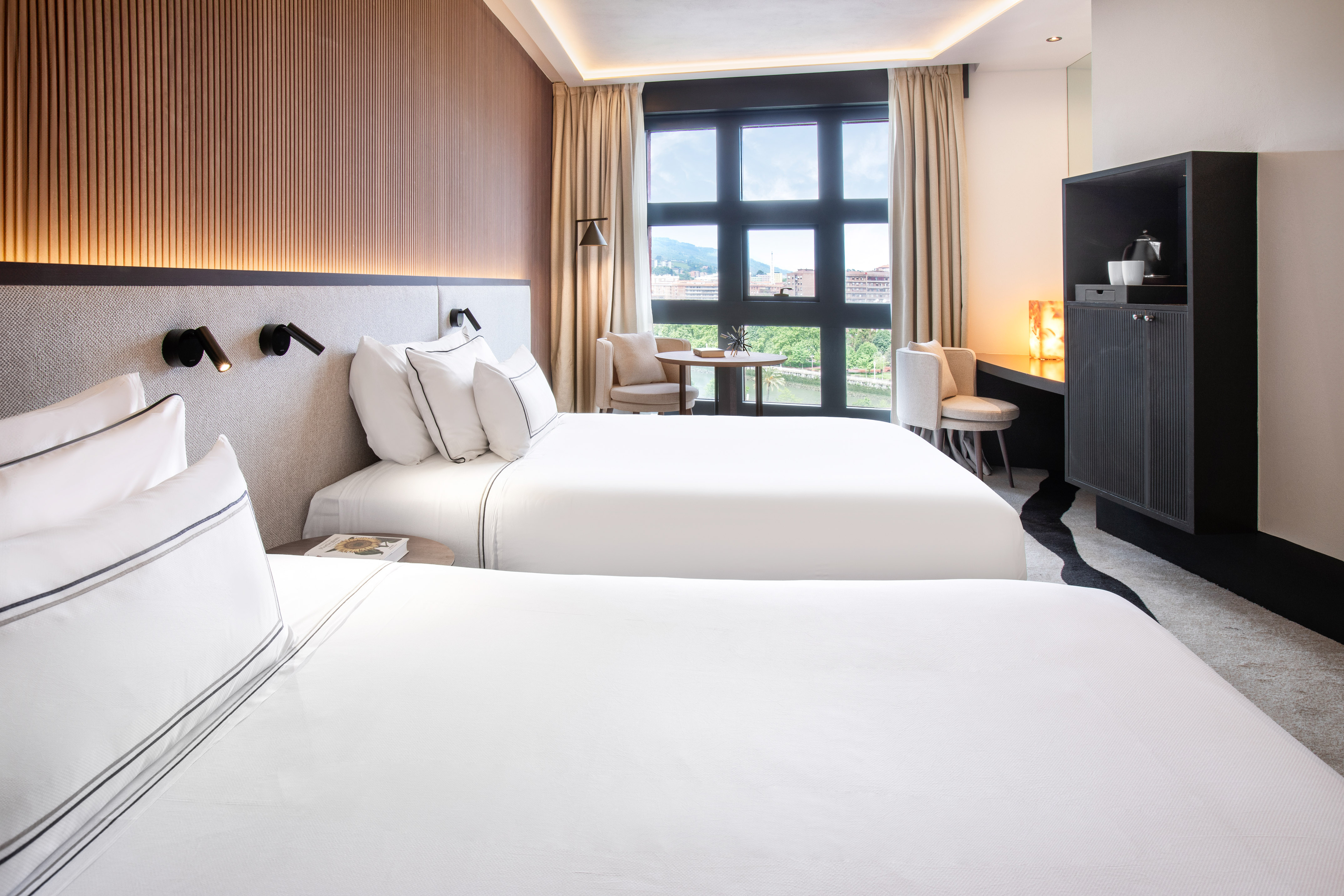 Luxury hotel room with two twin beds, modern decor, and a scenic window view.