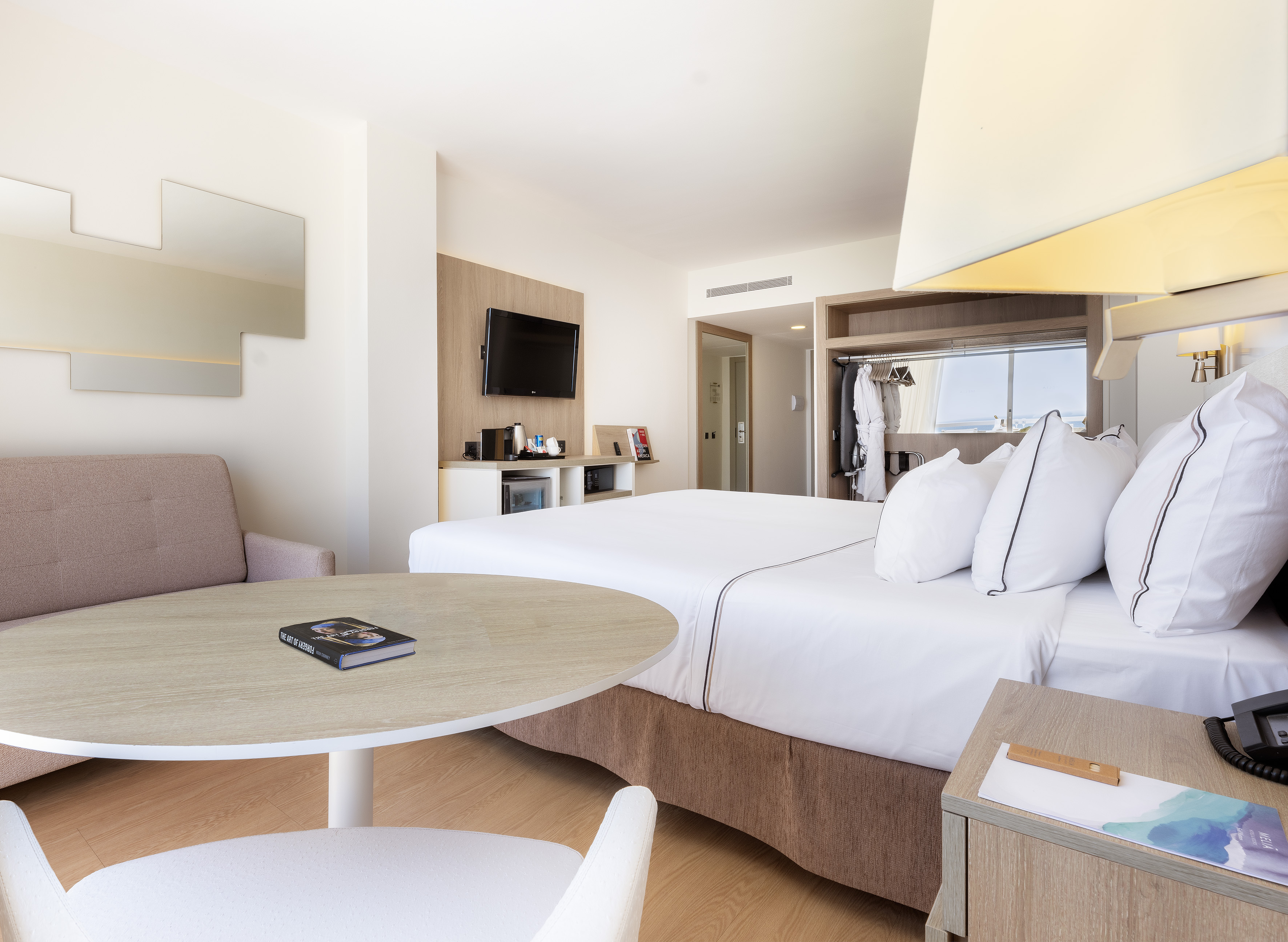Modern hotel room with king bed, sofa, TV, and open wardrobe.