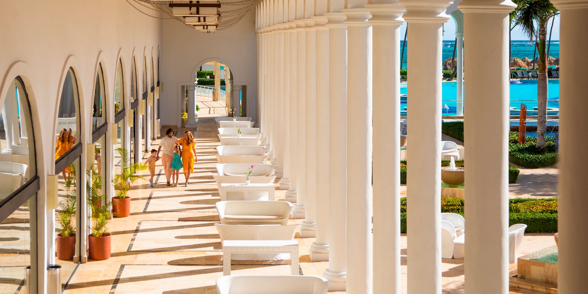 a group of people walking on a patio with white pillars