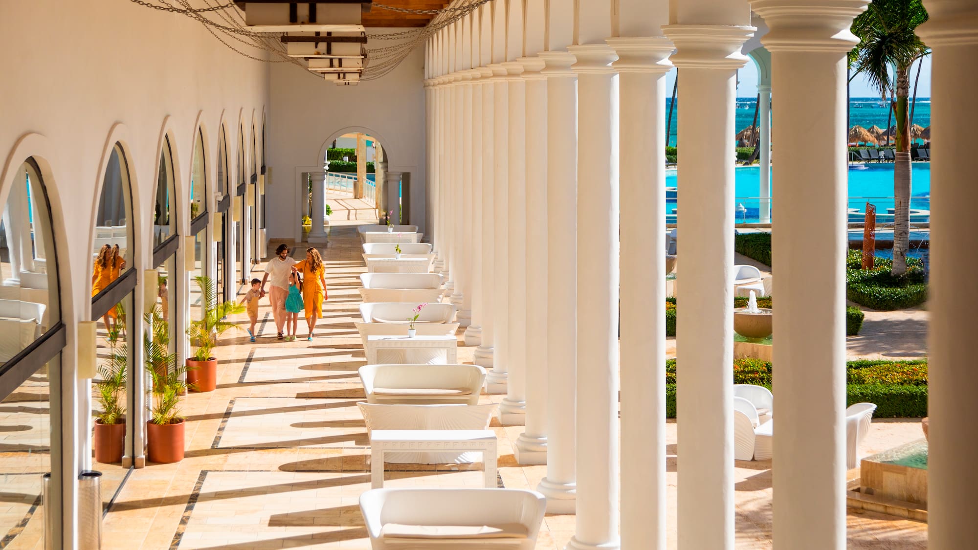 a group of people walking on a patio with white pillars