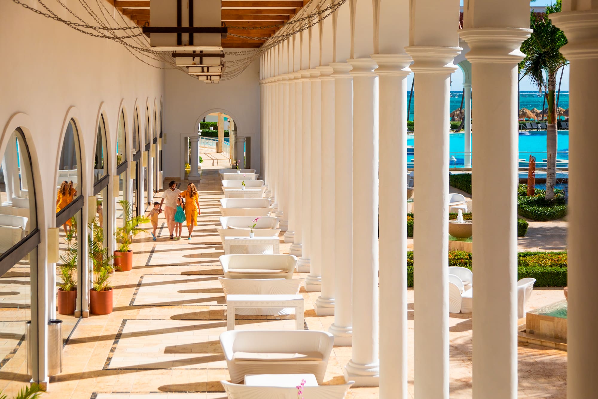 a group of people walking on a patio with white pillars