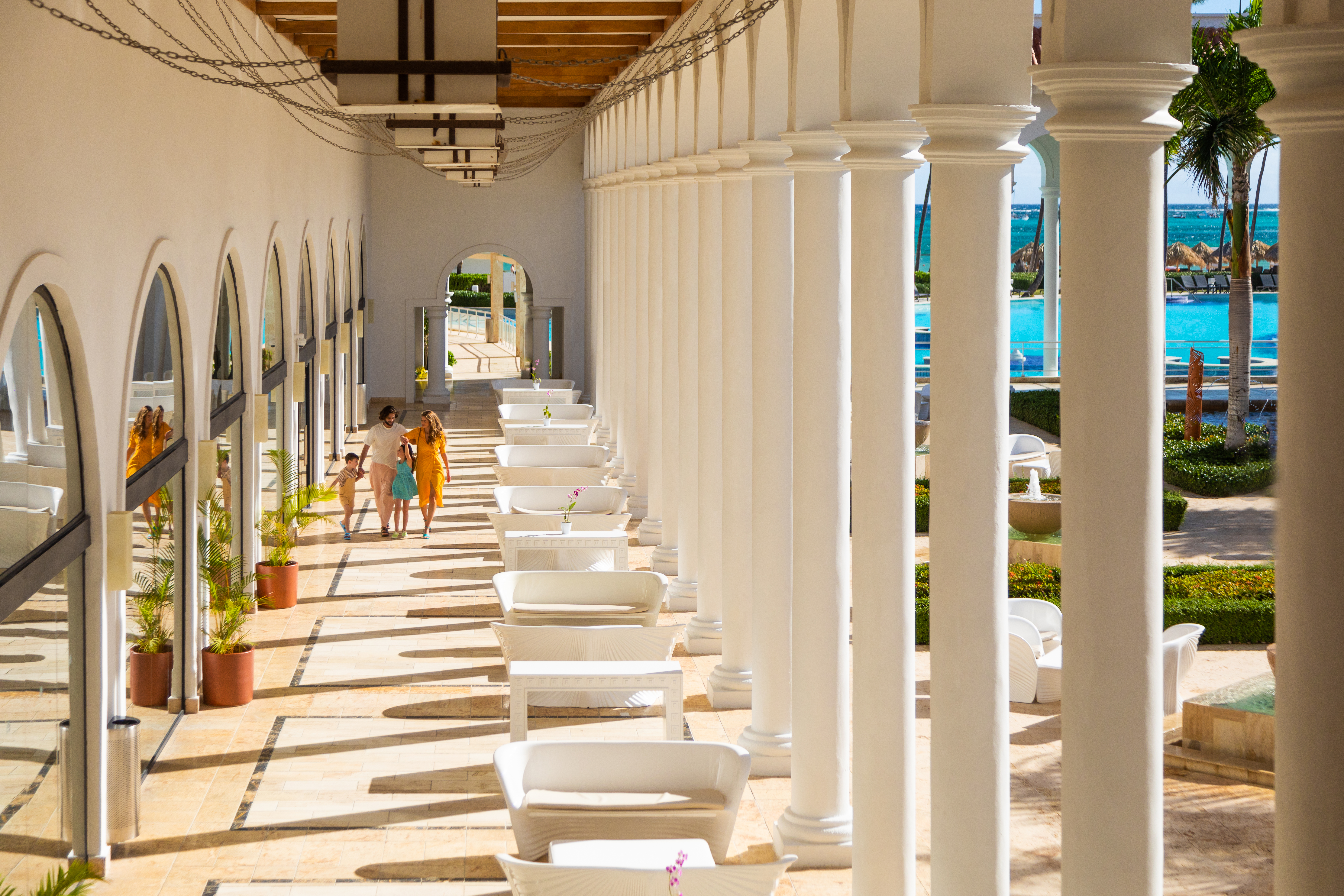Family walking in a resort's elegant hall with columns, pool, and ocean.