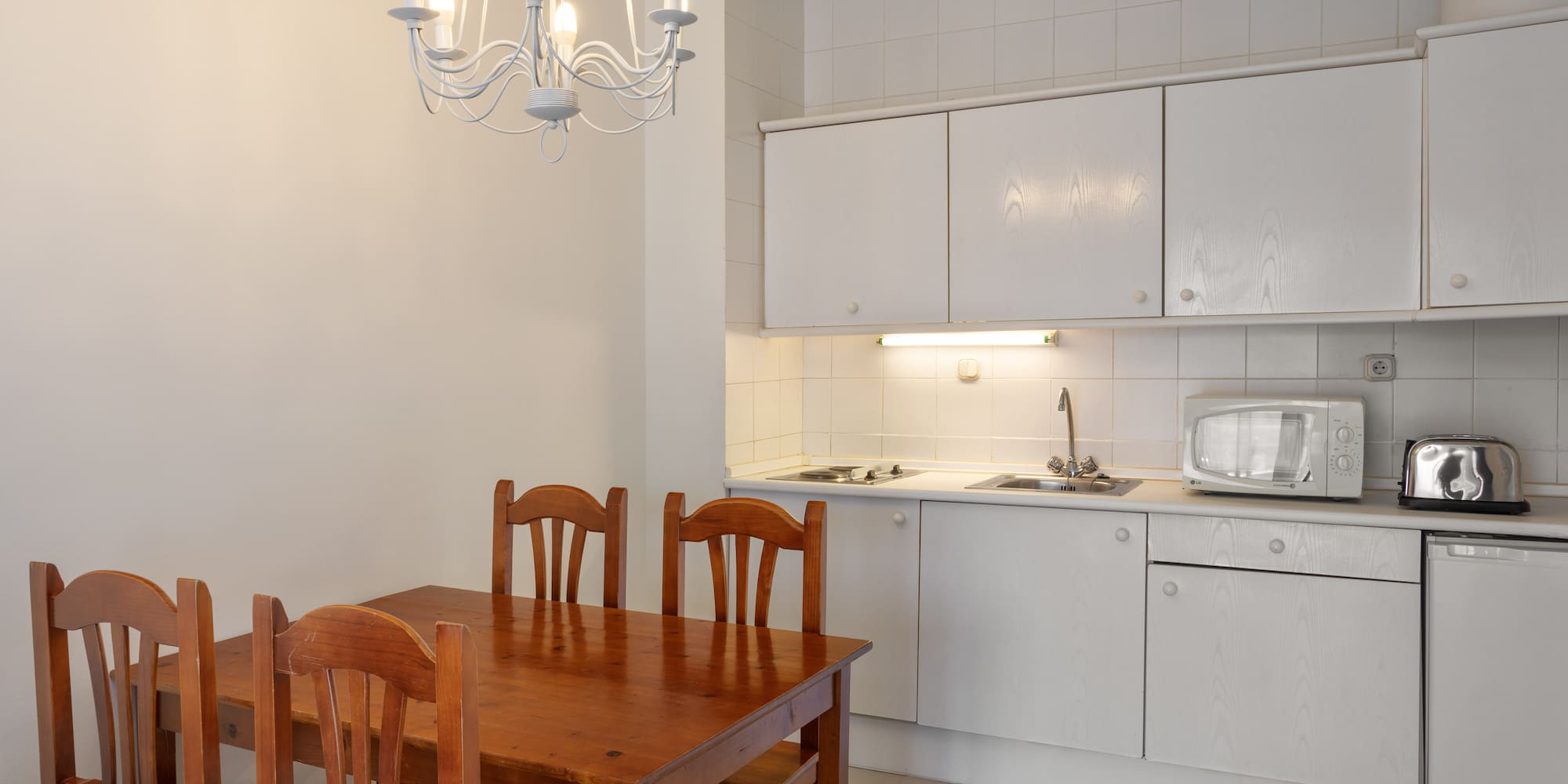 Kitchen dining area with wooden table, white cabinets, microwave, and chandelier.