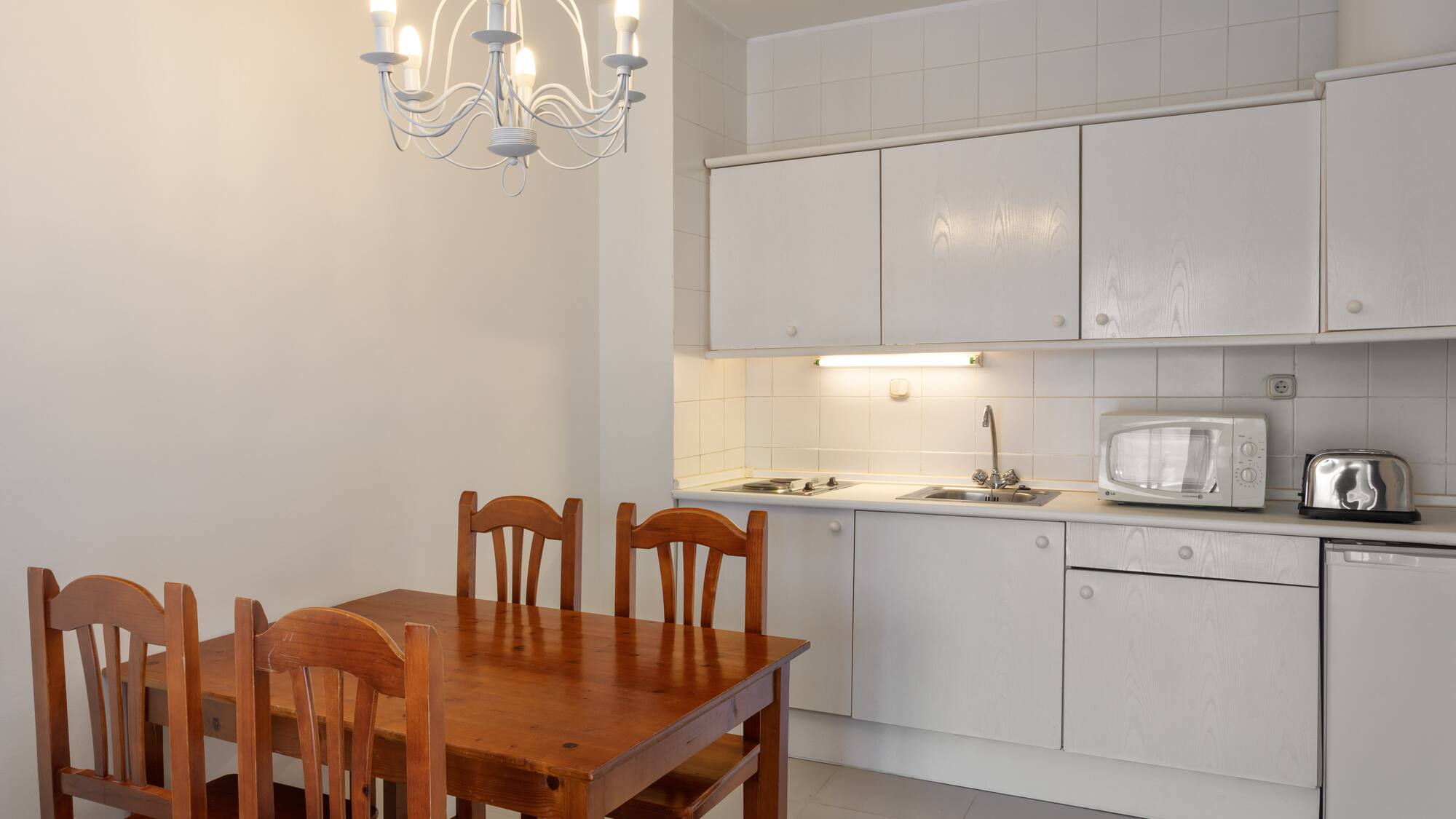 Kitchen dining area with wooden table, white cabinets, microwave, and chandelier.