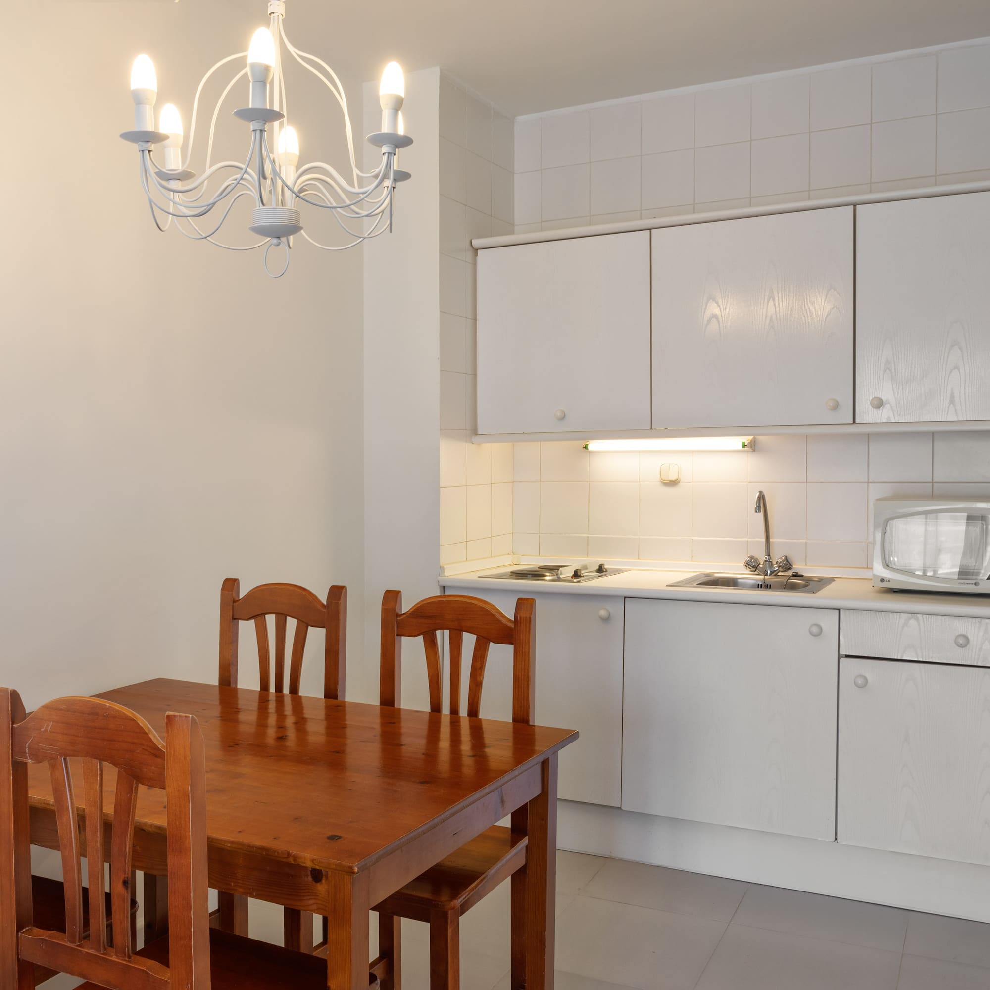 Kitchen dining area with wooden table, white cabinets, microwave, and chandelier.