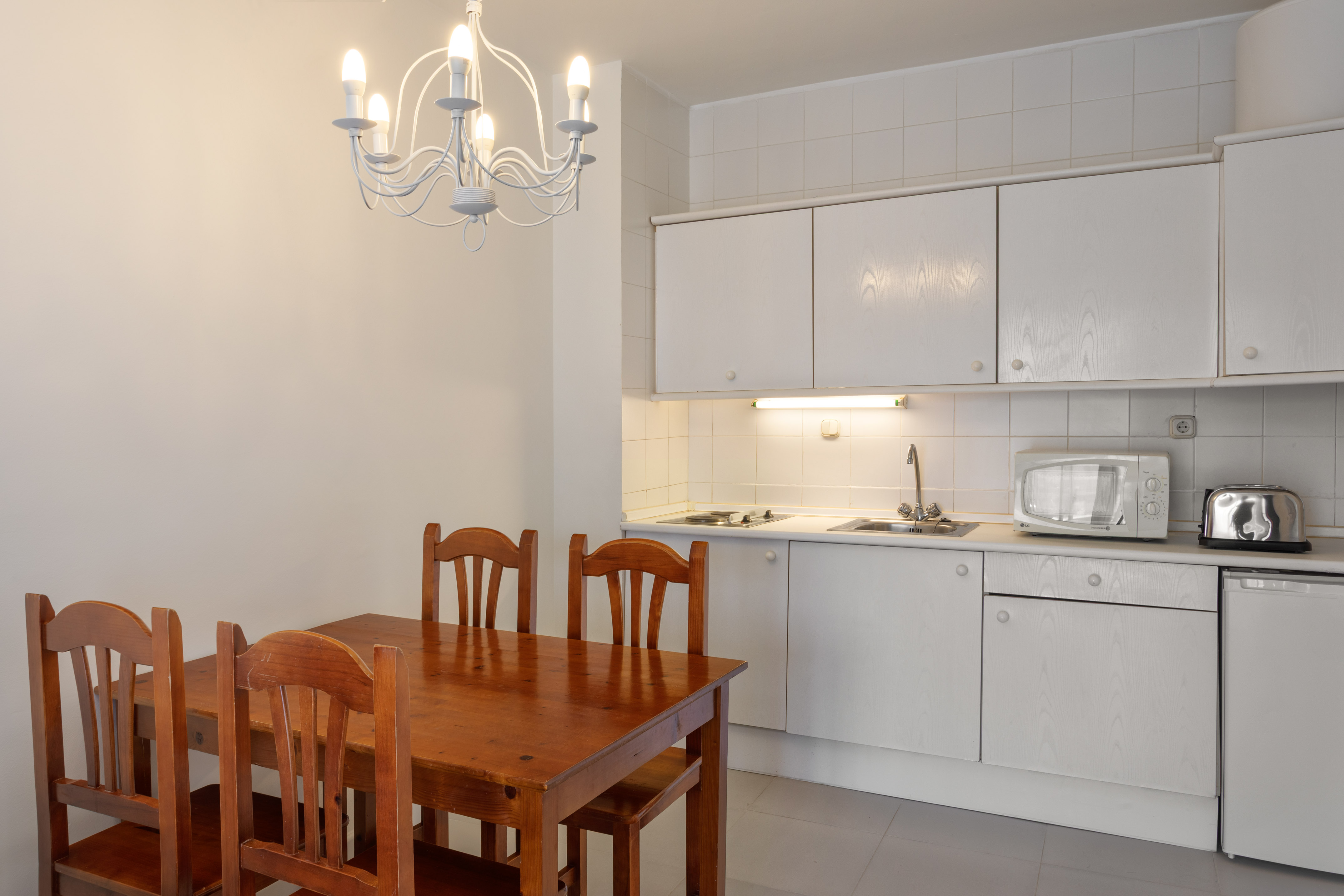 Kitchen dining area with wooden table, white cabinets, microwave, and chandelier.