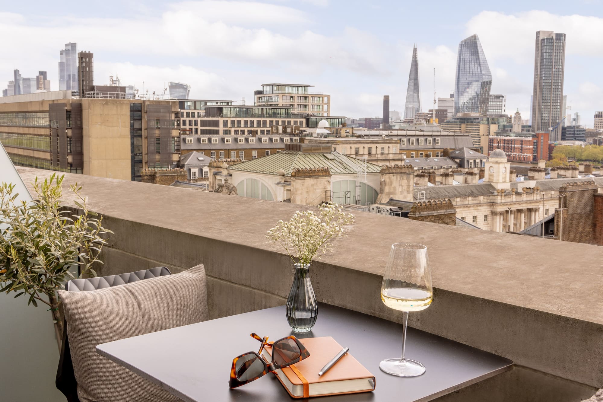 A balcony with a table holding glasses and books, framed by a city skyline in the background.