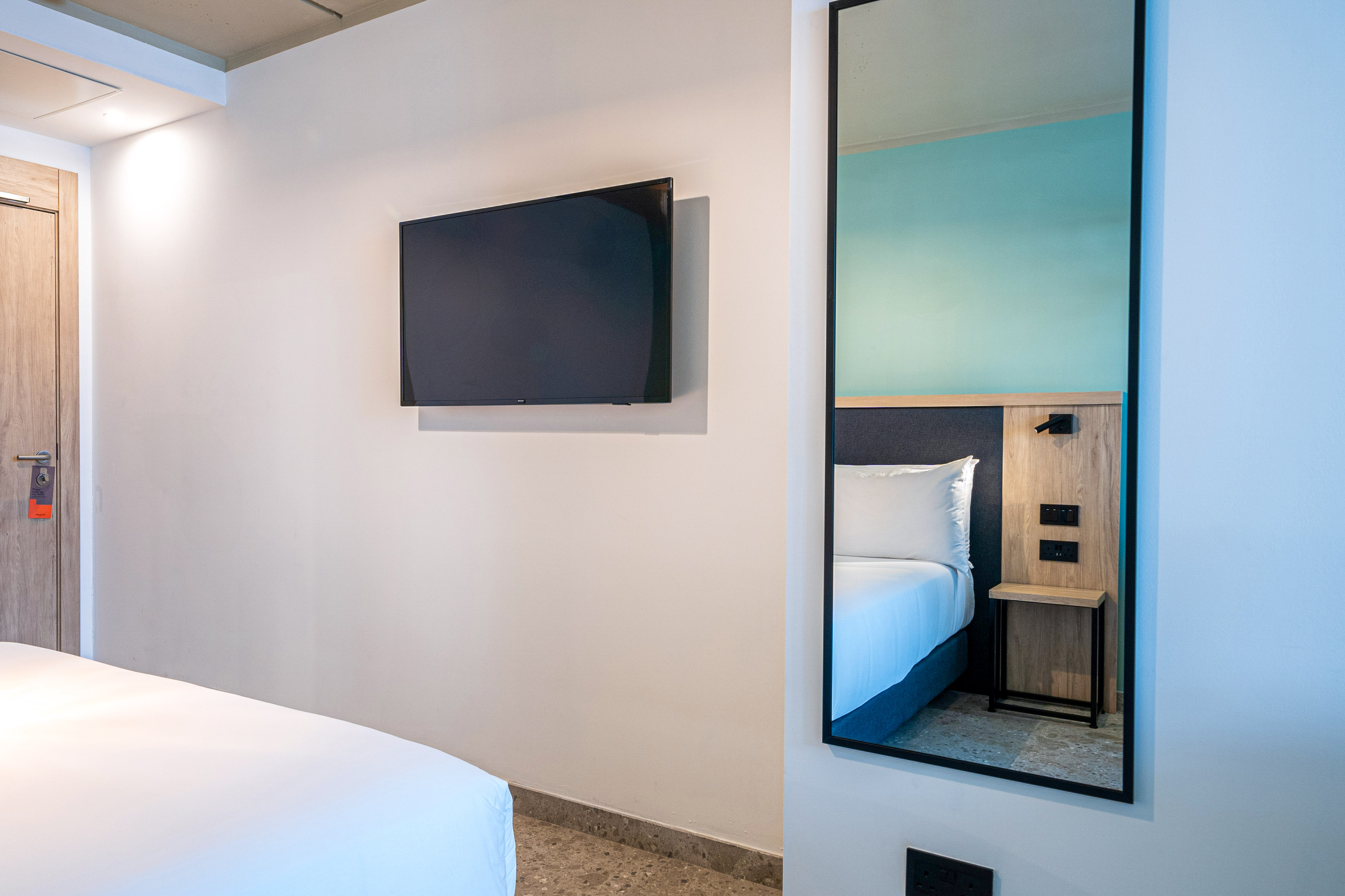 Modern hotel room with wall TV and mirror reflecting bed.