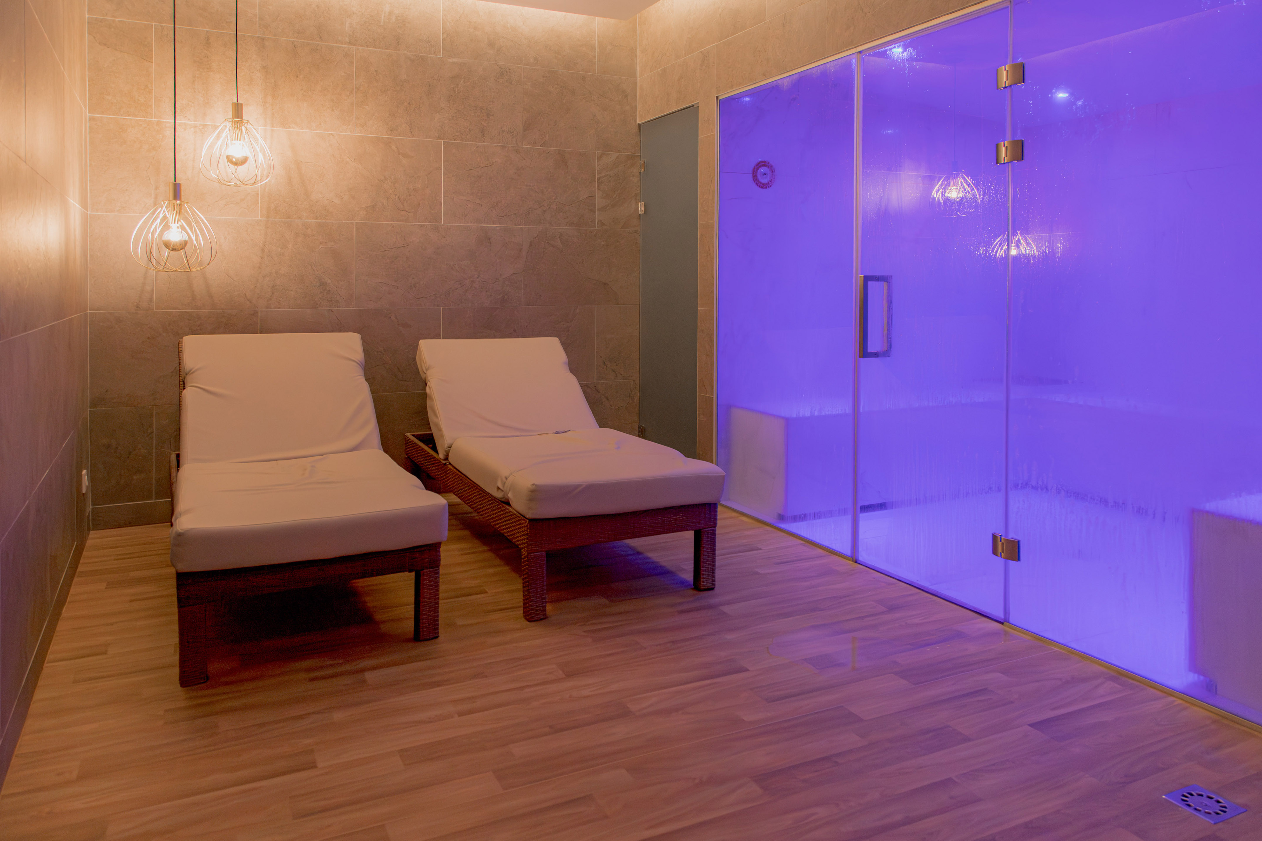Spa lounge chairs beside a purple-lit steam room with tiled walls.