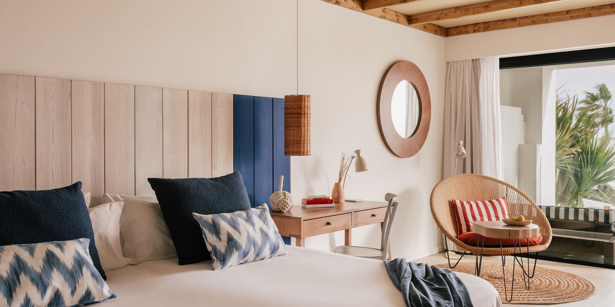 Habitación costera con cama, cabecero de madera, escritorio y sillón de ratán.