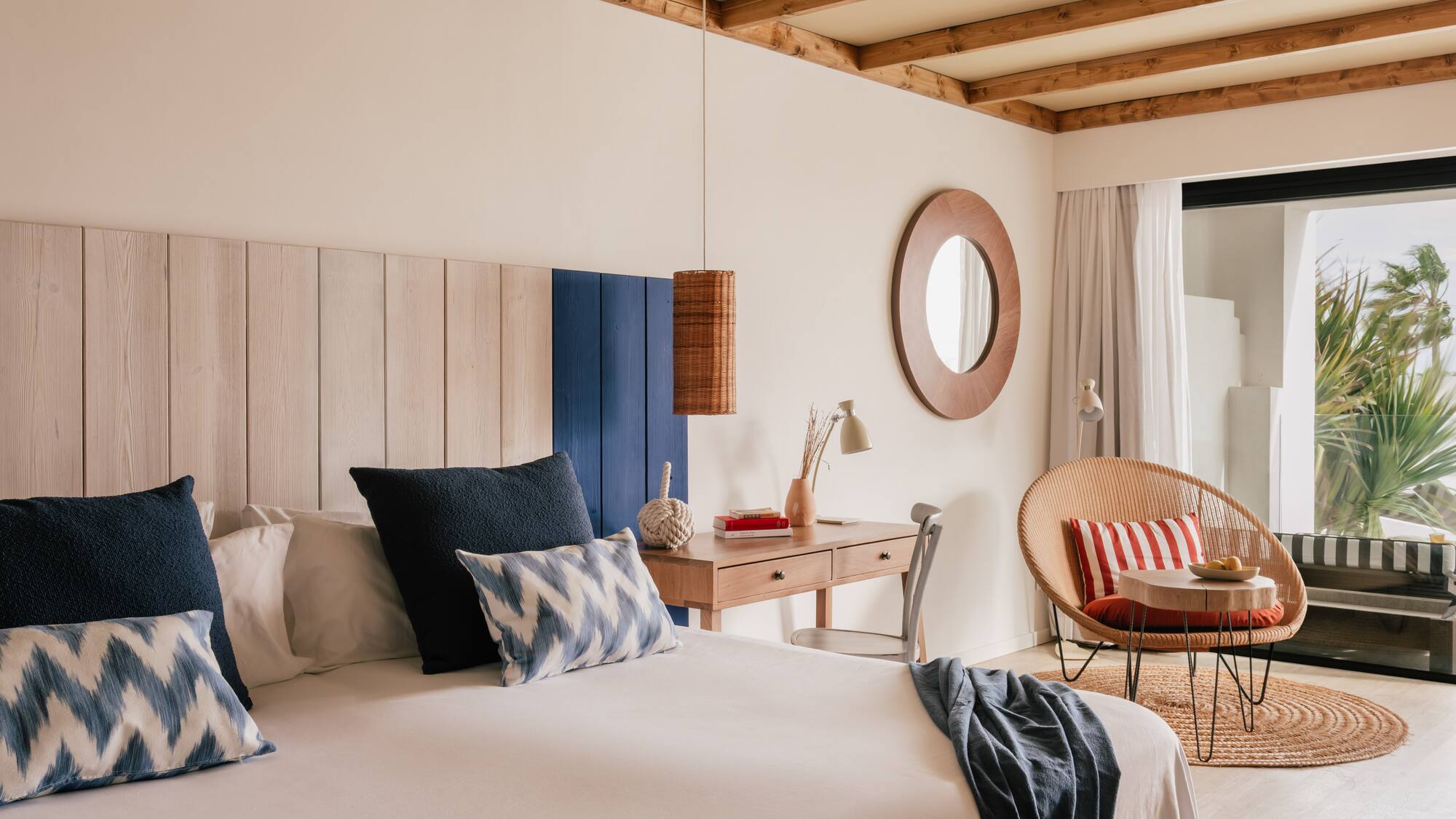 Habitación costera con cama, cabecero de madera, escritorio y sillón de ratán.