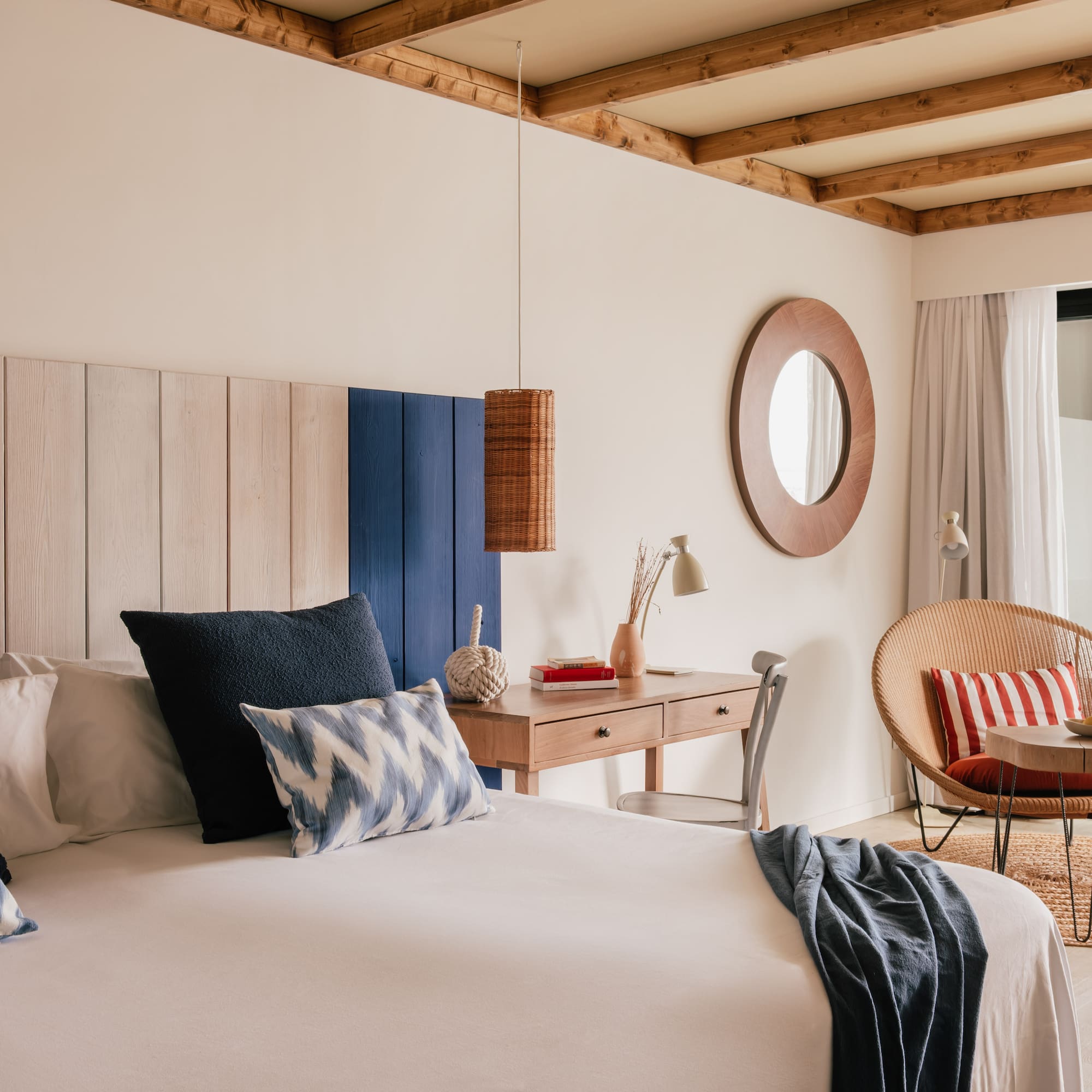 Habitación costera con cama, cabecero de madera, escritorio y sillón de ratán.