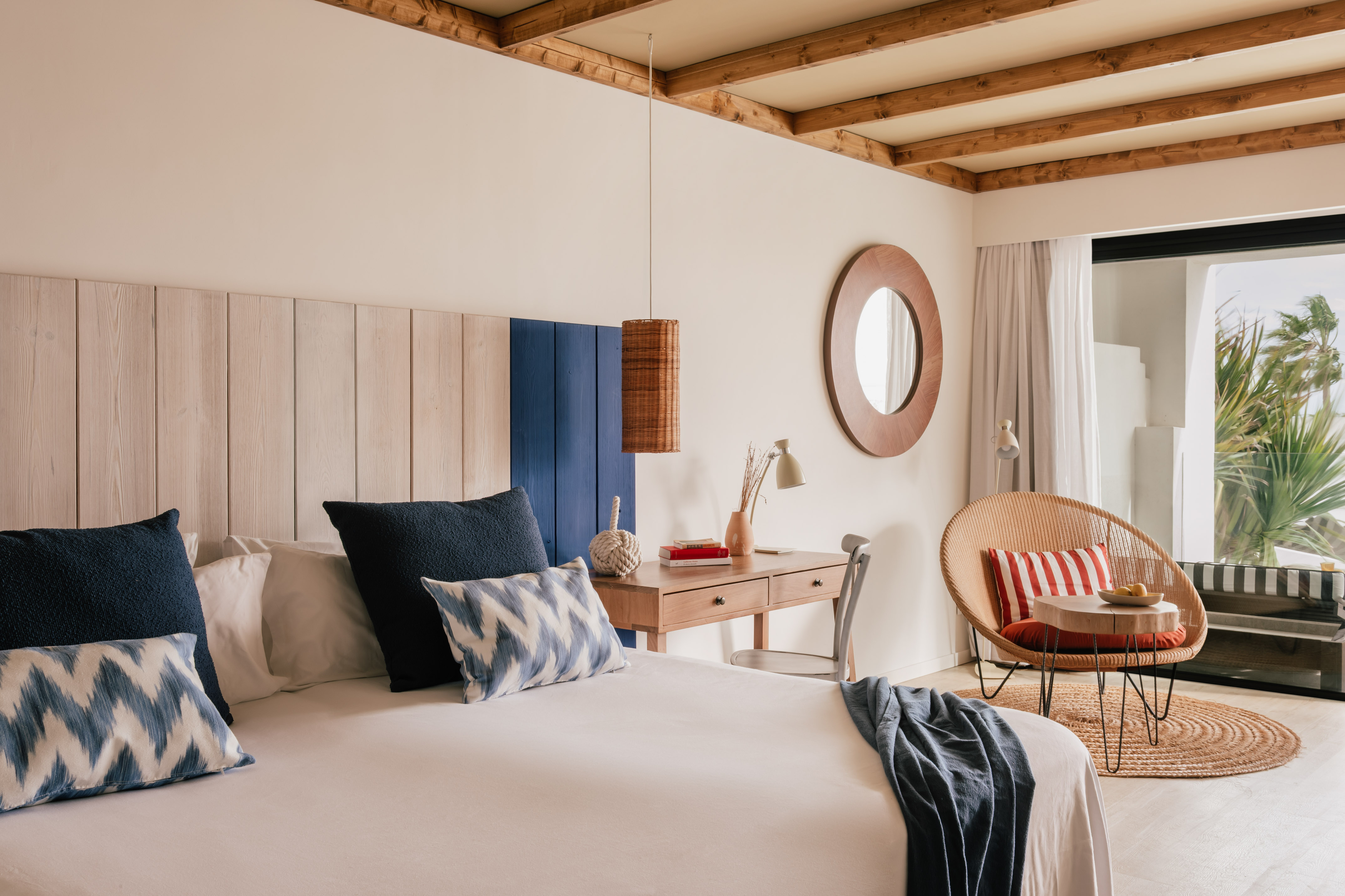 Habitación costera con cama, cabecero de madera, escritorio y sillón de ratán.