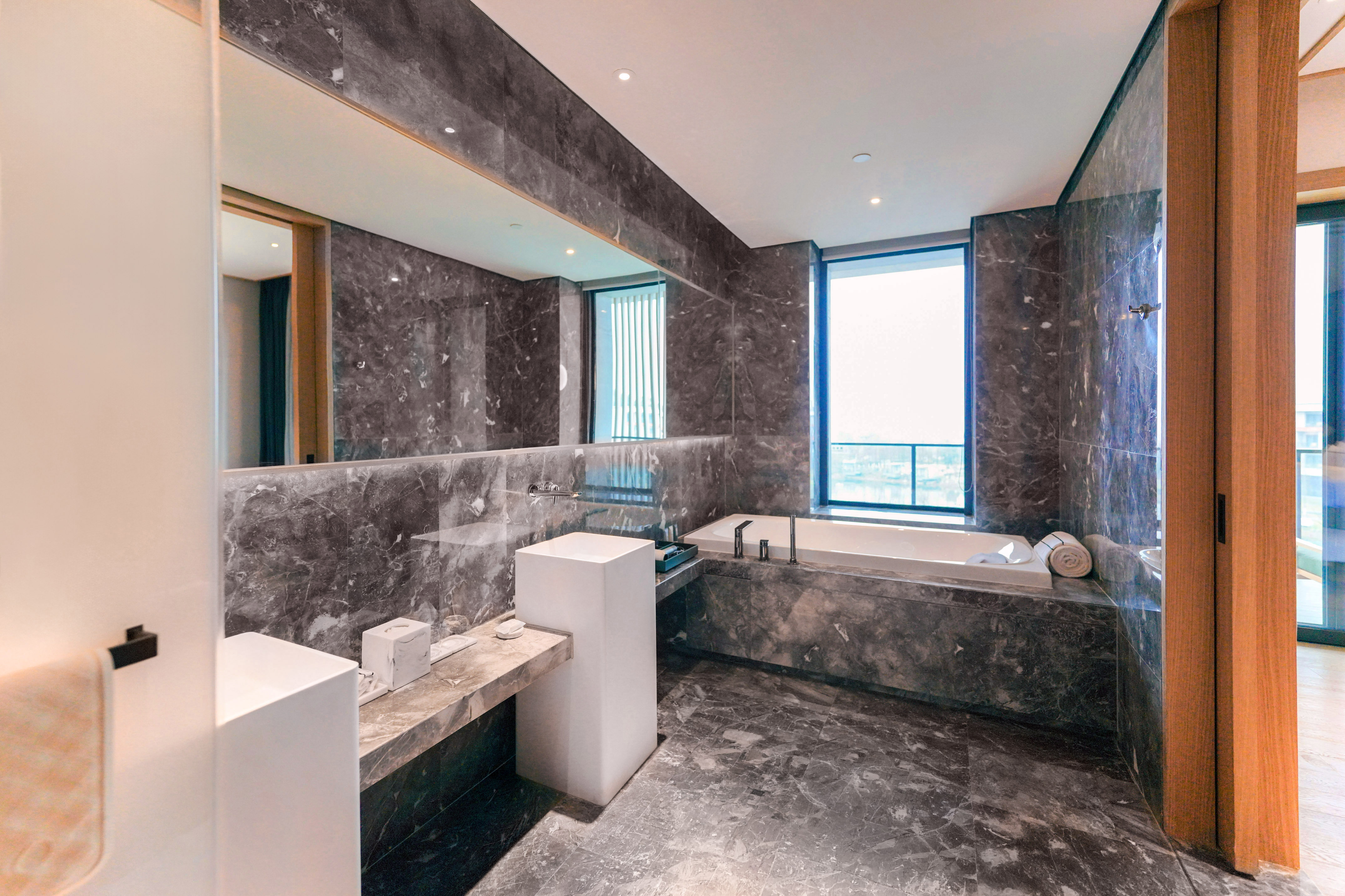 Modern luxury bathroom with dark marble, deep bathtub, and sleek white sink.