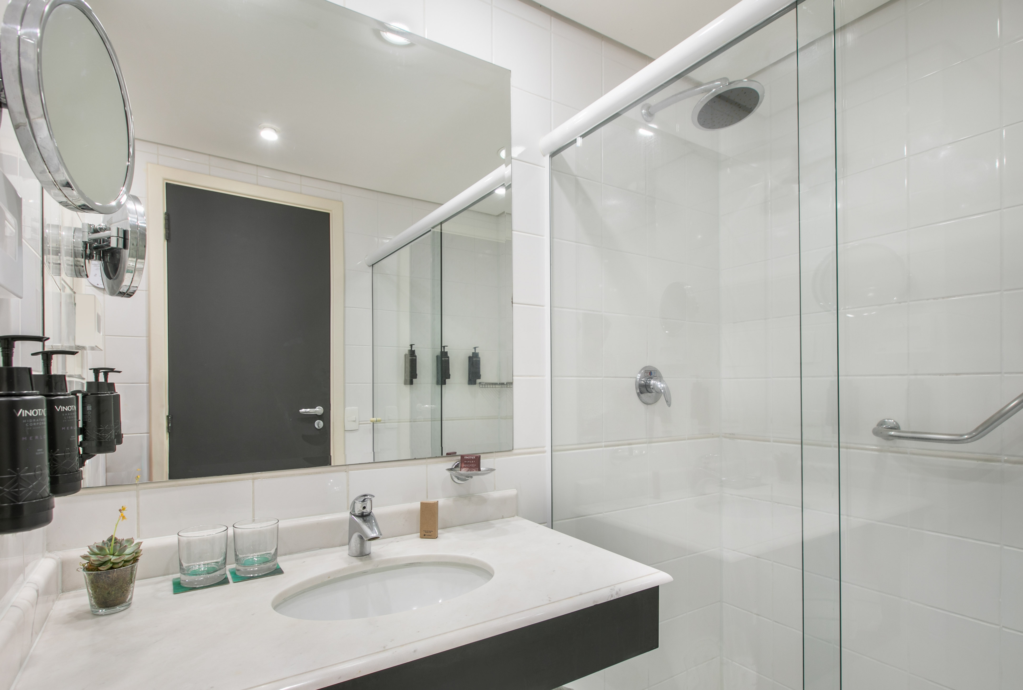 Modern hotel bathroom with white tiles, glass shower, vanity, and mirror.