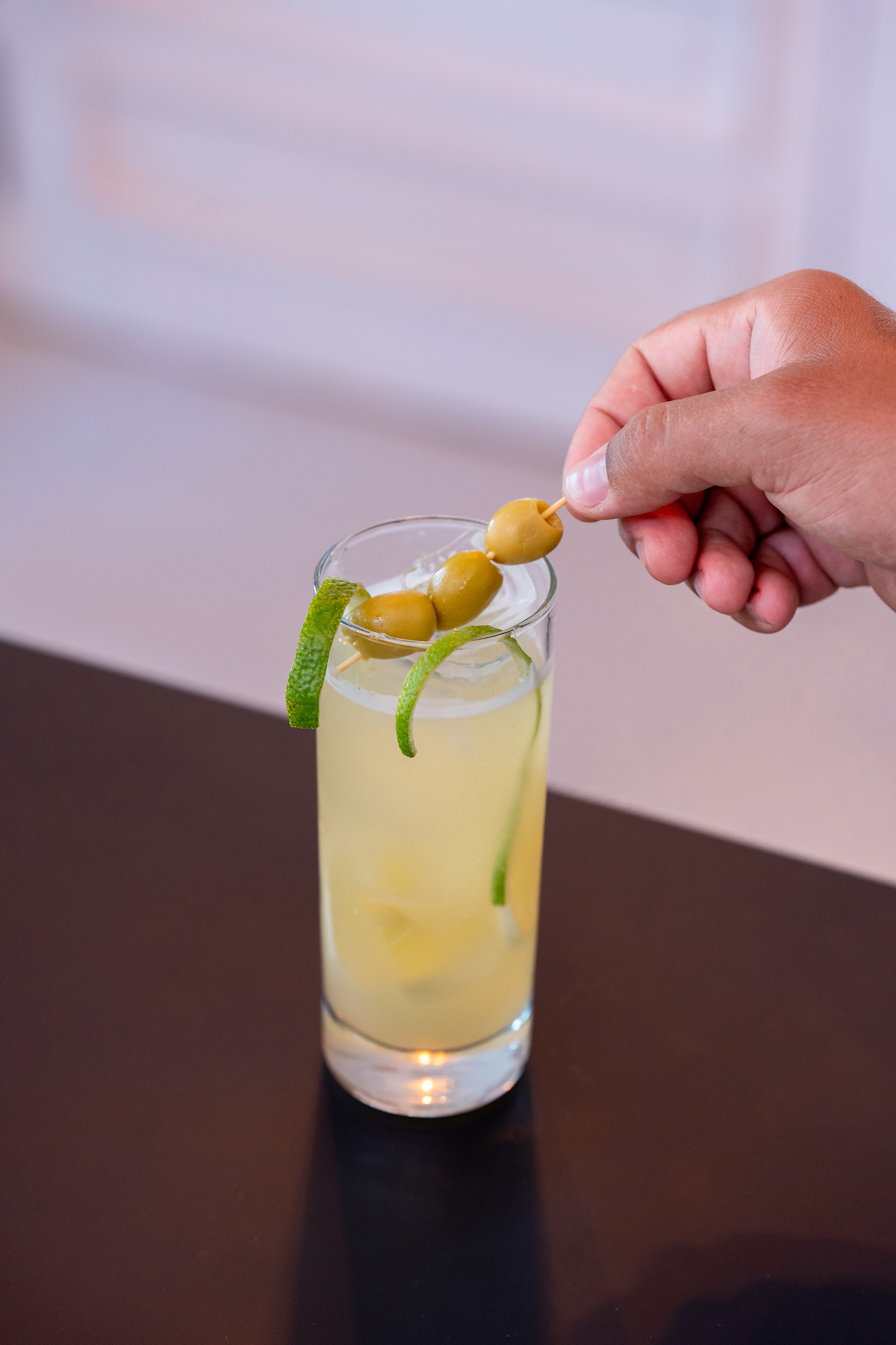 a hand holding a stick with olives on a stick in a glass of liquid