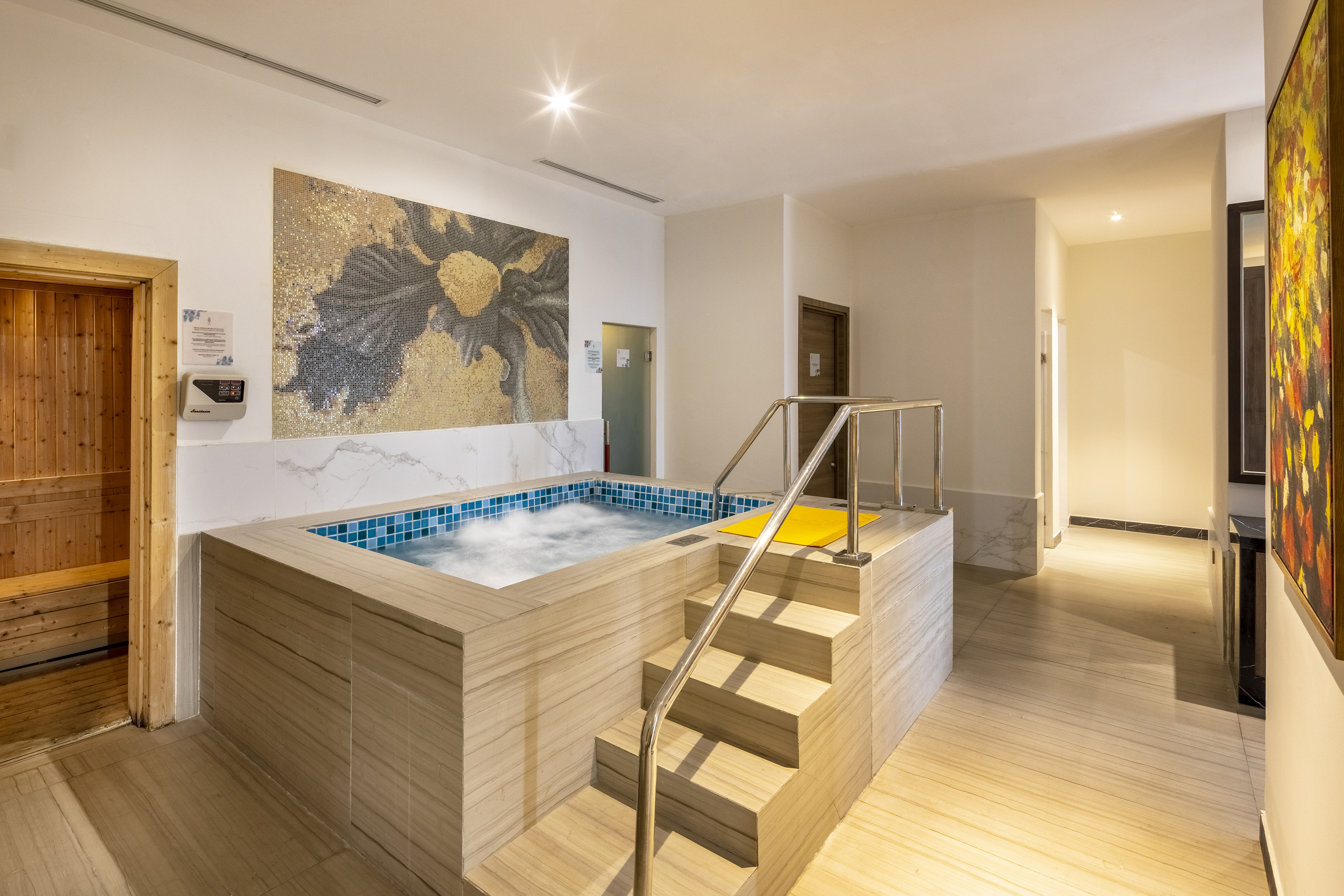 Indoor spa with bubbling hot tub, wooden sauna, and mosaic wall art. - YHI Spa - Meliá Vinpearl Thanh Hoa, Thanh Hoa