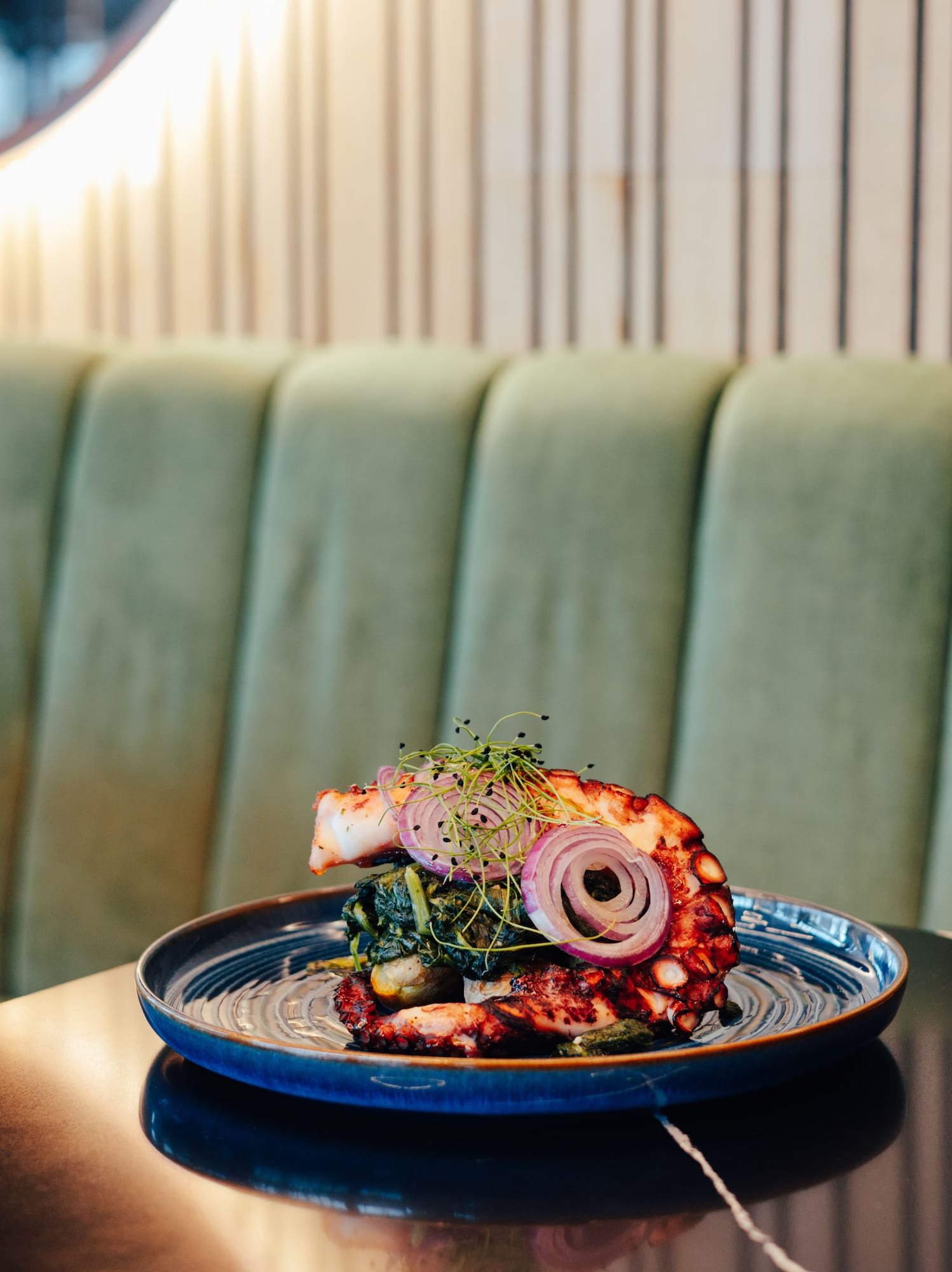 Grilled octopus with red onion, greens, and microgreens at a restaurant.