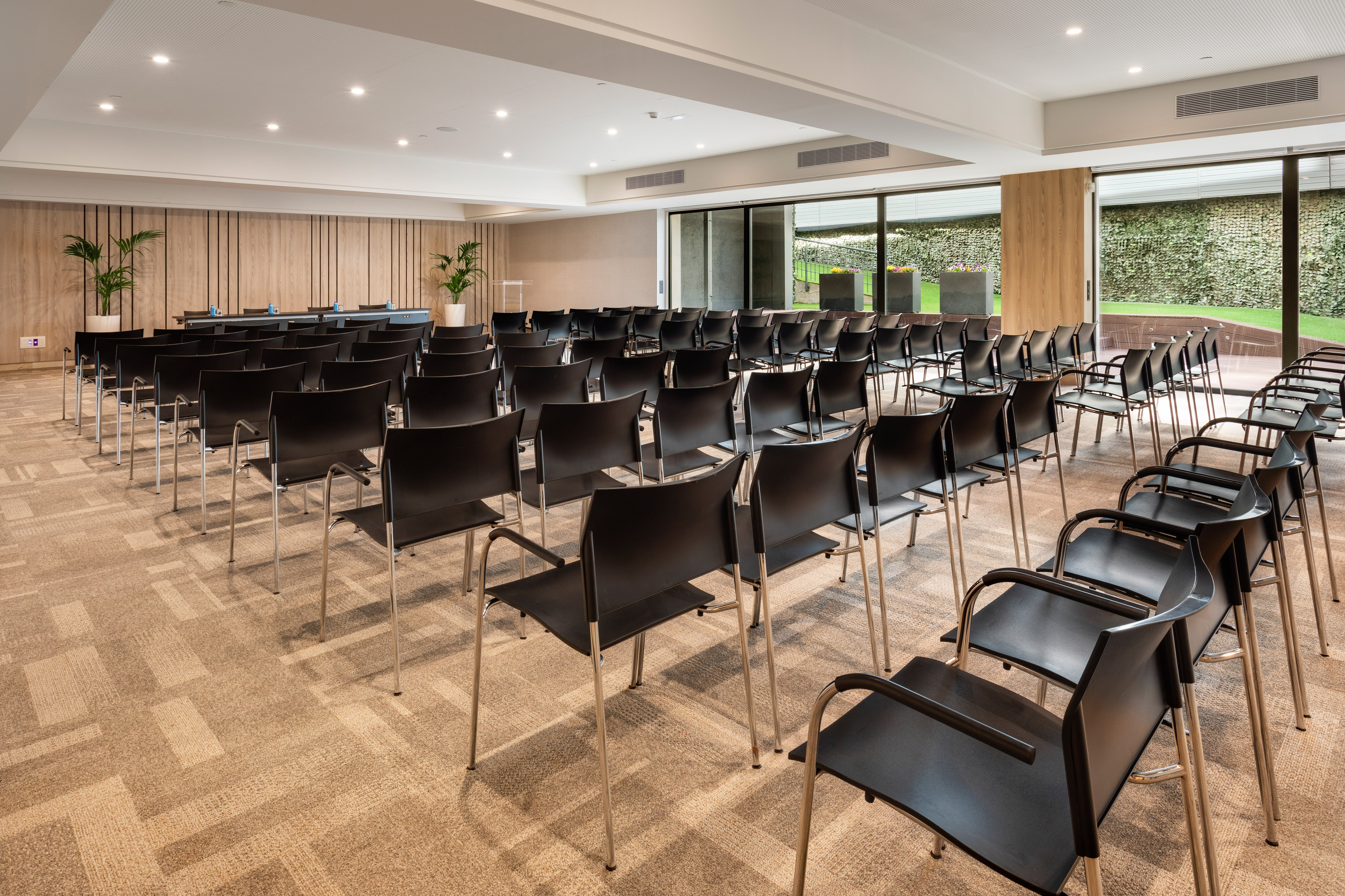 Modern meeting room with black chairs, wood accents, and green garden view.