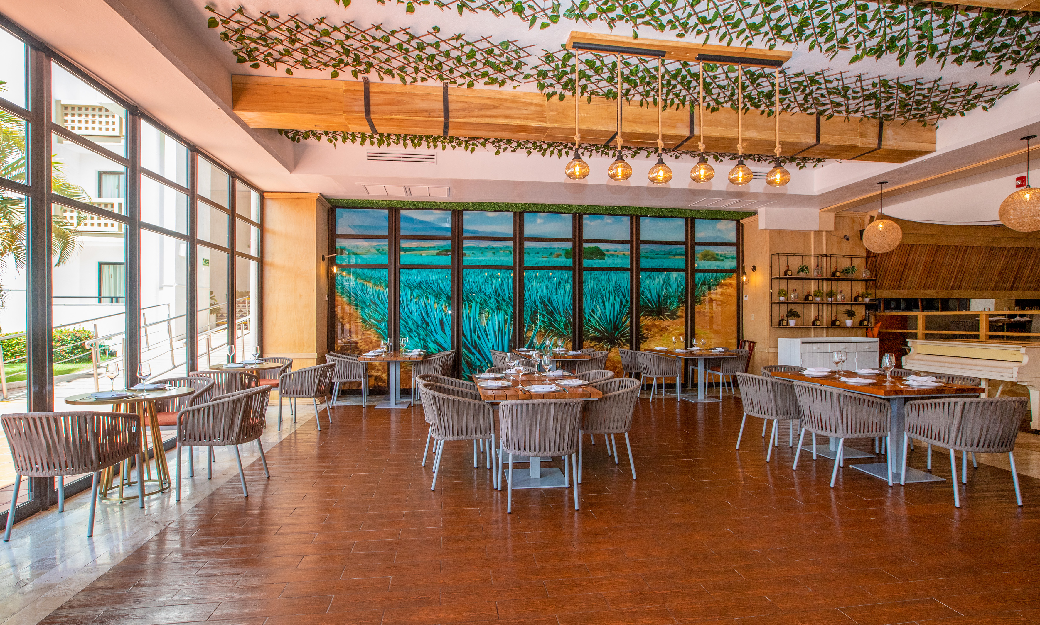 Modern resort restaurant with agave mural, sleek tables, and vine ceiling decor.