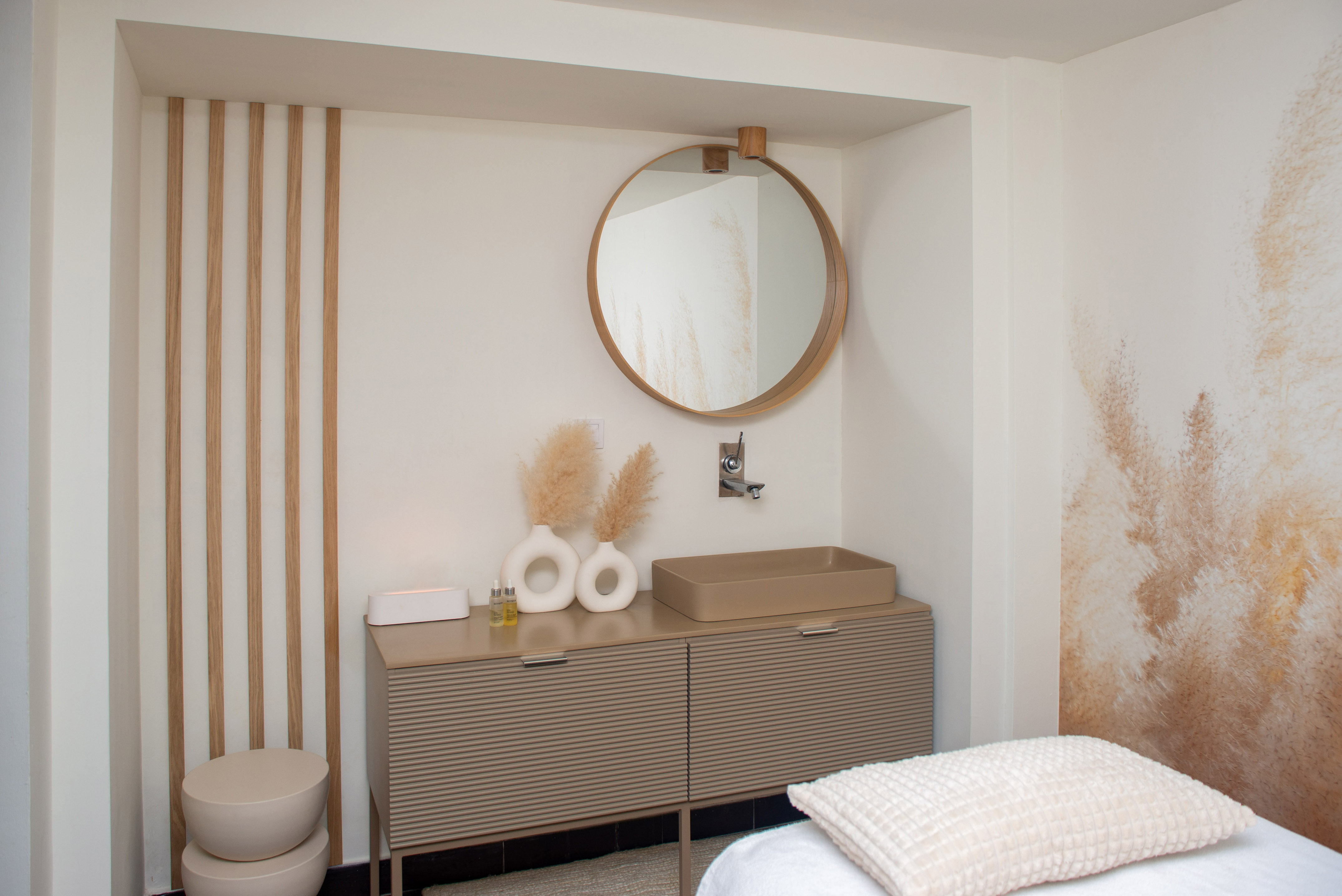 Minimalist spa bathroom with round wood mirror, beige vanity, and pampas grass decor.