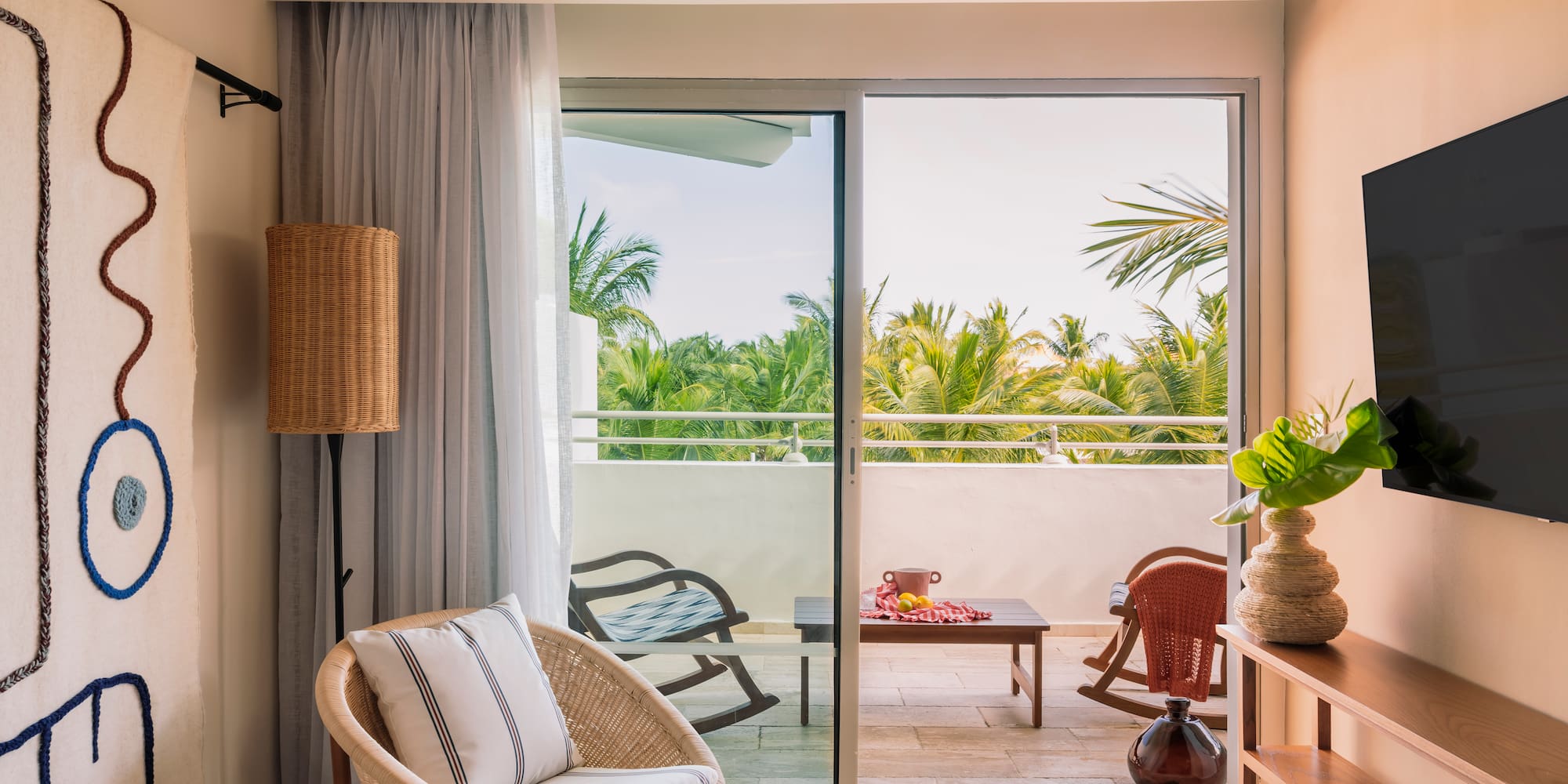 Tropical hotel suite living room with wicker chair, balcony, and palm view.