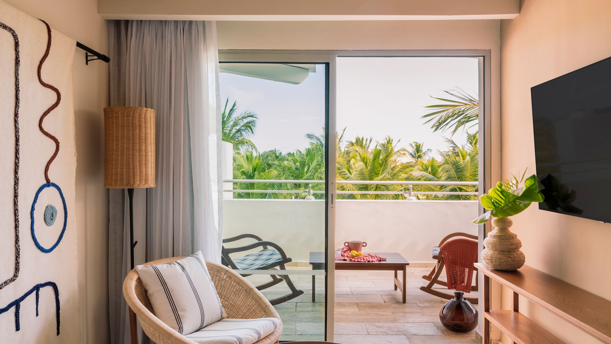 Tropical hotel suite living room with wicker chair, balcony, and palm view.