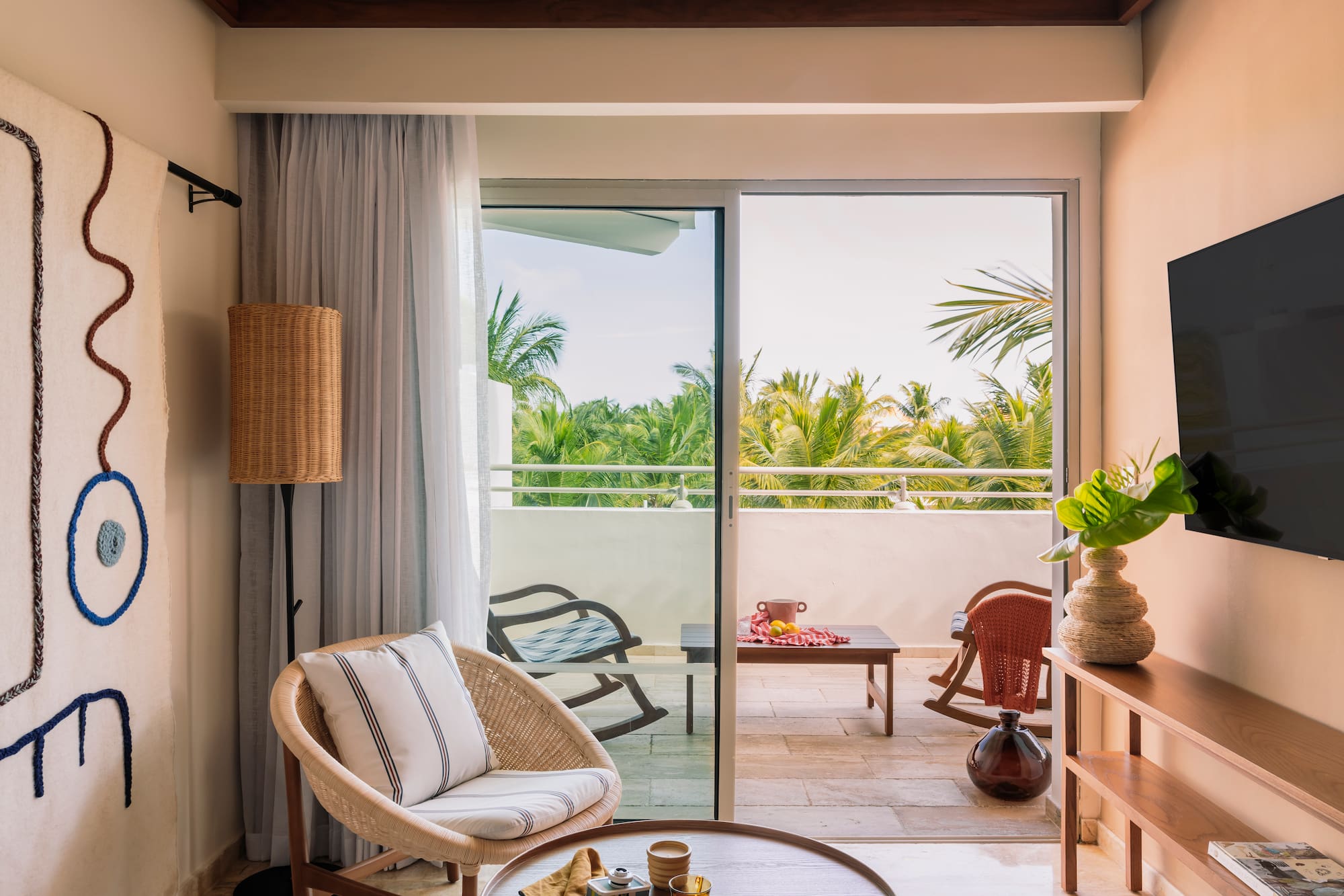 Tropical hotel suite living room with wicker chair, balcony, and palm view.