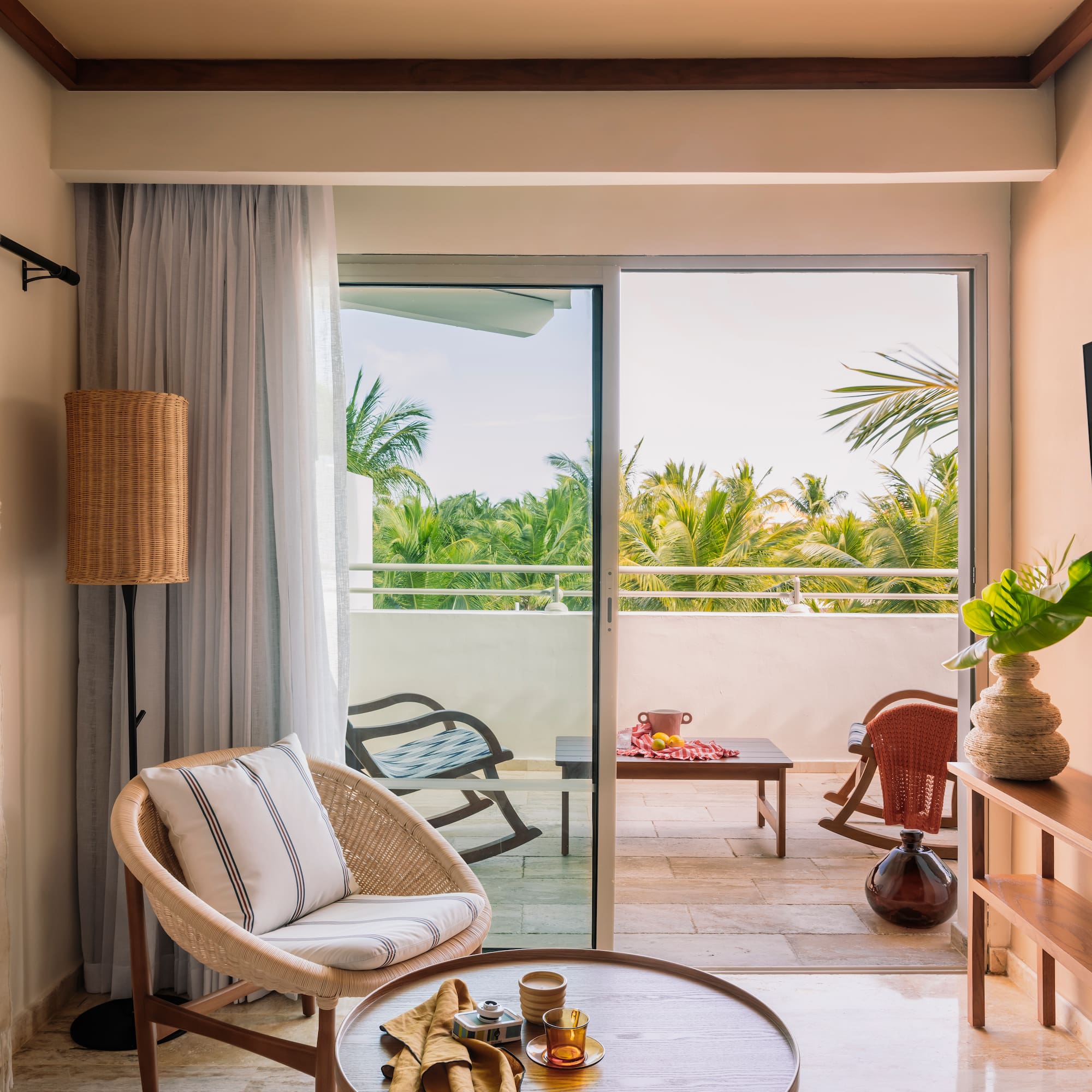 Tropical hotel suite living room with wicker chair, balcony, and palm view.