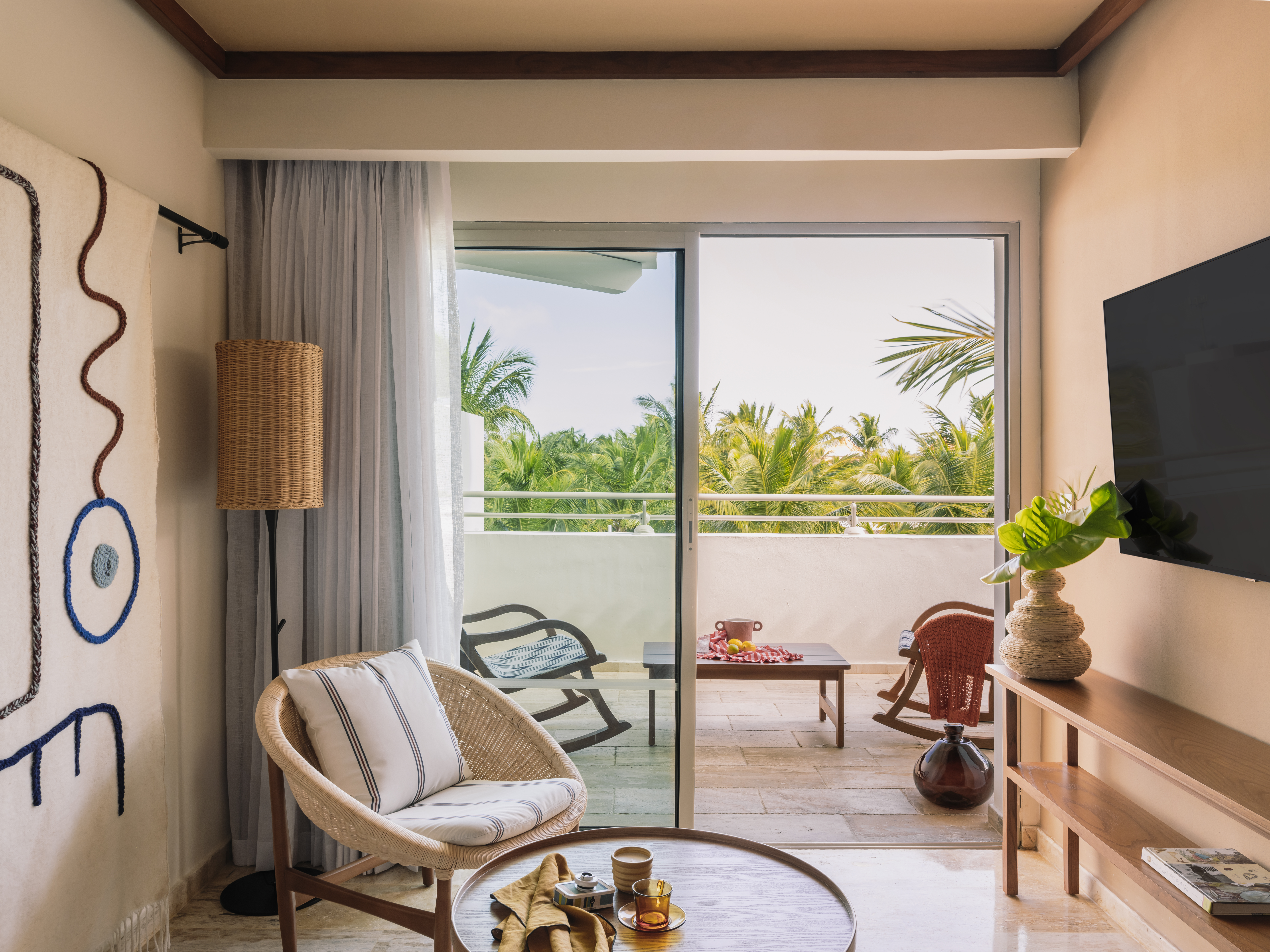 Tropical hotel suite living room with wicker chair, balcony, and palm view.