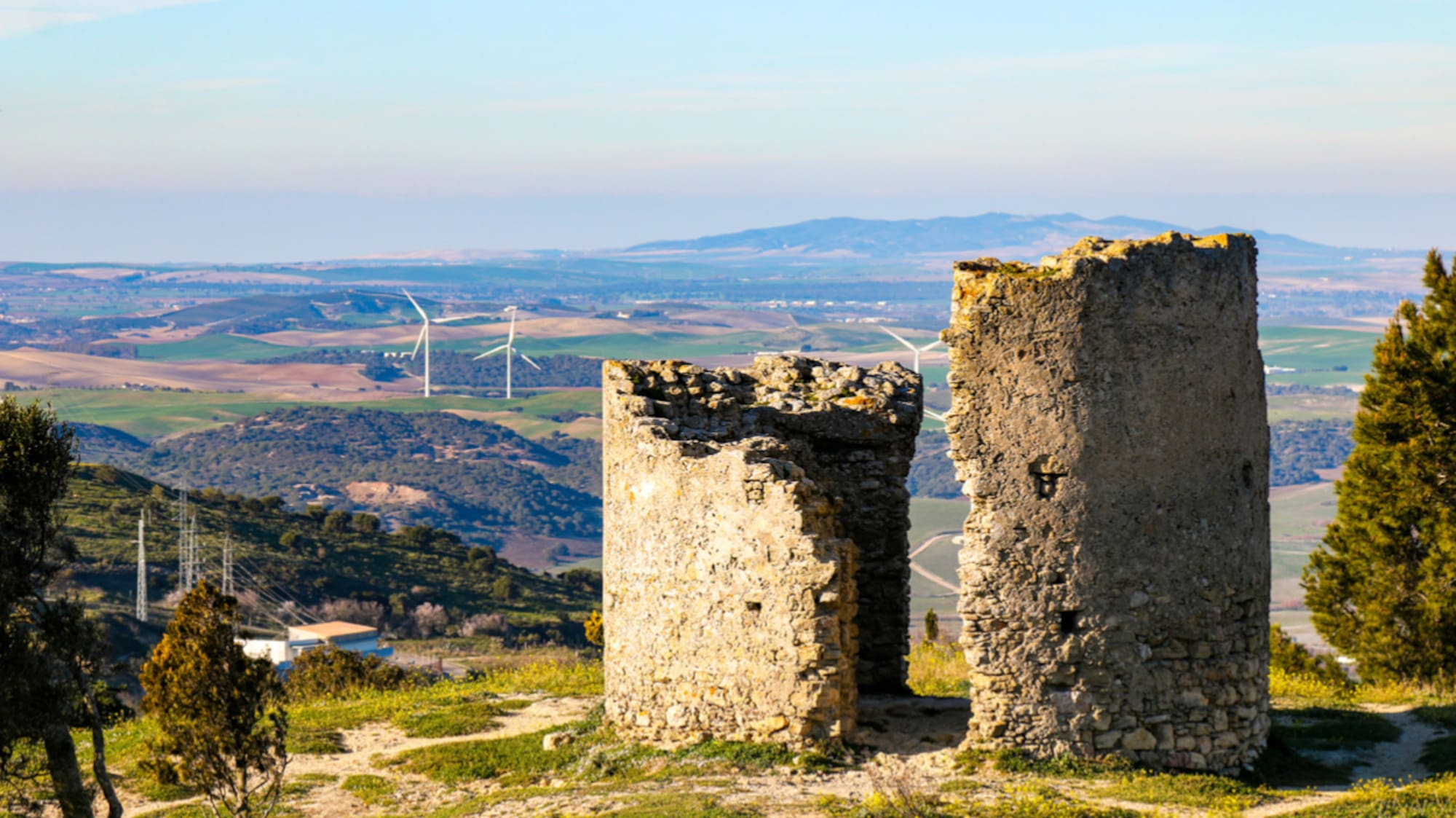 a stone ruins on a hill with wind turbines in the background