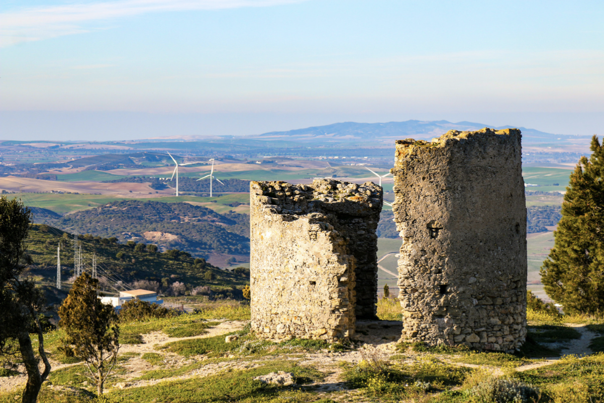 a stone ruins on a hill with wind turbines in the background