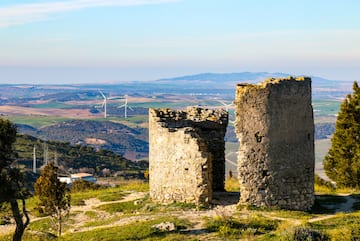 a stone ruins on a hill with wind turbines in the background