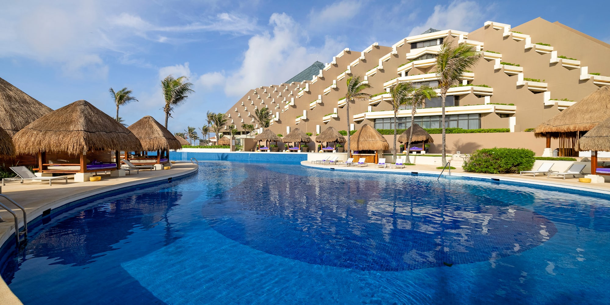 a pool with straw umbrellas and a building in the background